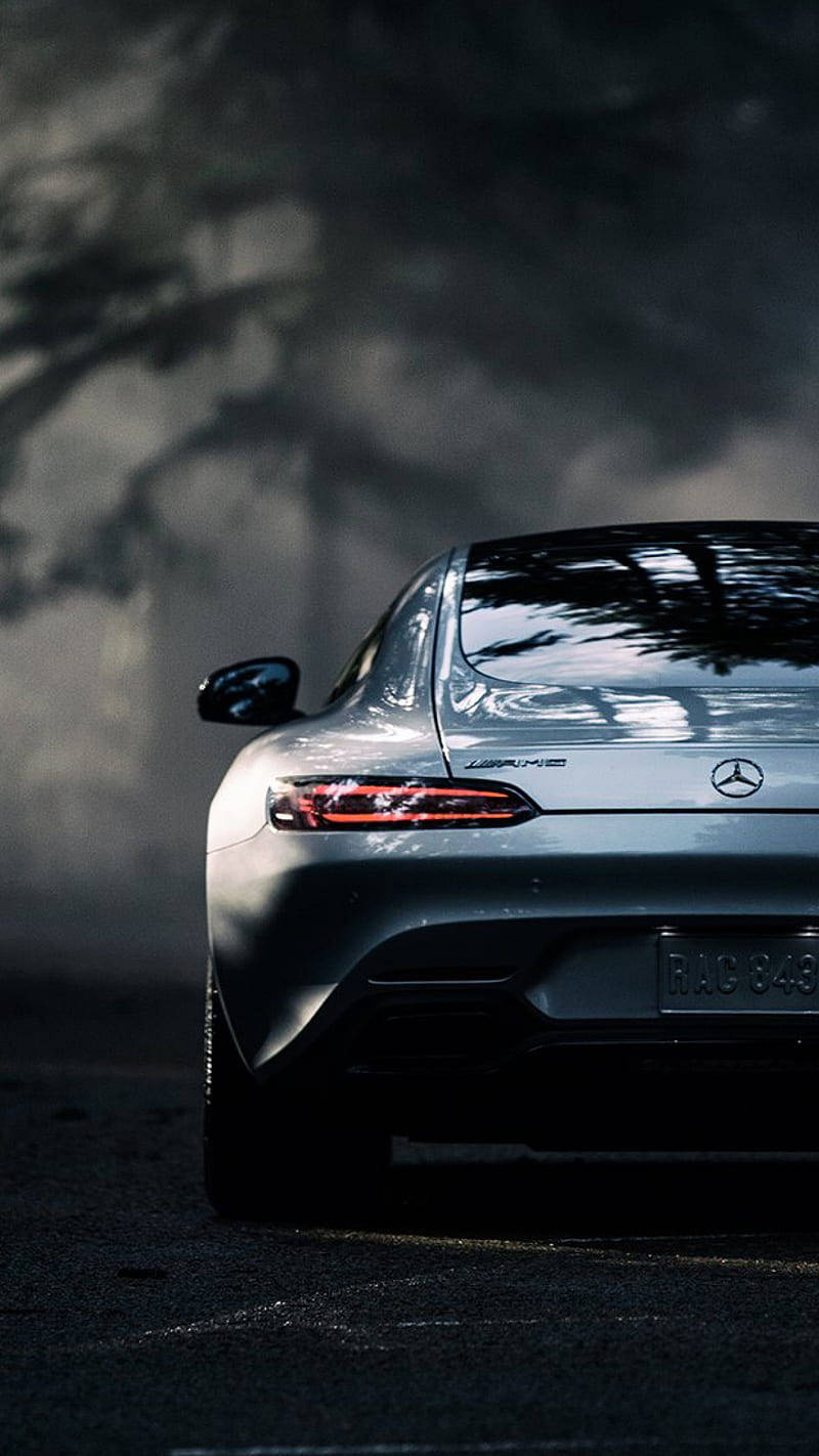 Mercedes 桌布 壁紙 — 一輛時尚的銀色 Mercedes-AMG 跑車停放在戲劇性的風暴雲下，樹影投射在車尾。