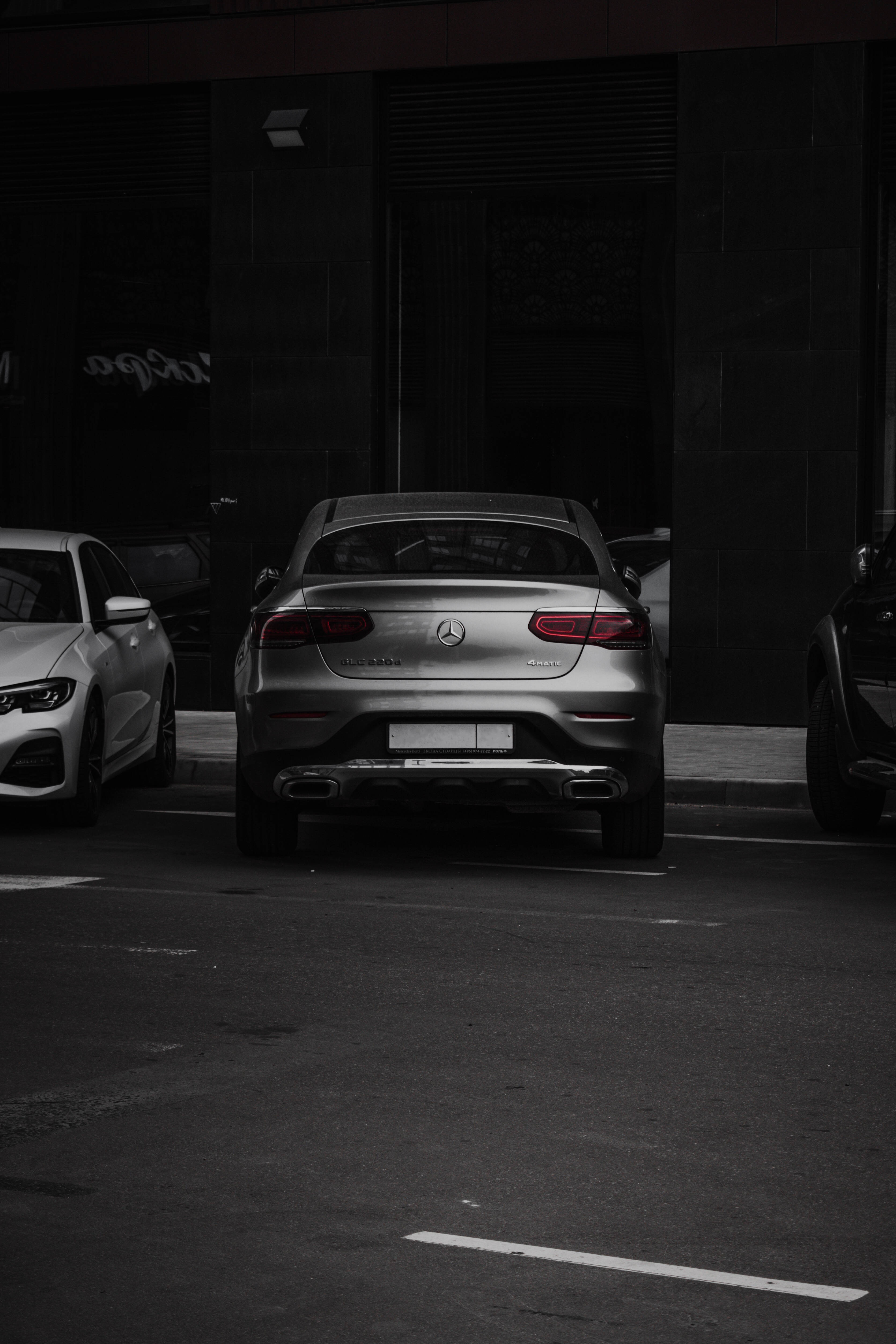 amg iPhone 桌布 壁紙 — 一輛時尚的銀色 Mercedes-Benz 轎車停放在光線昏暗的城市地段，帶有鮮明的陰影和柔和的色調。