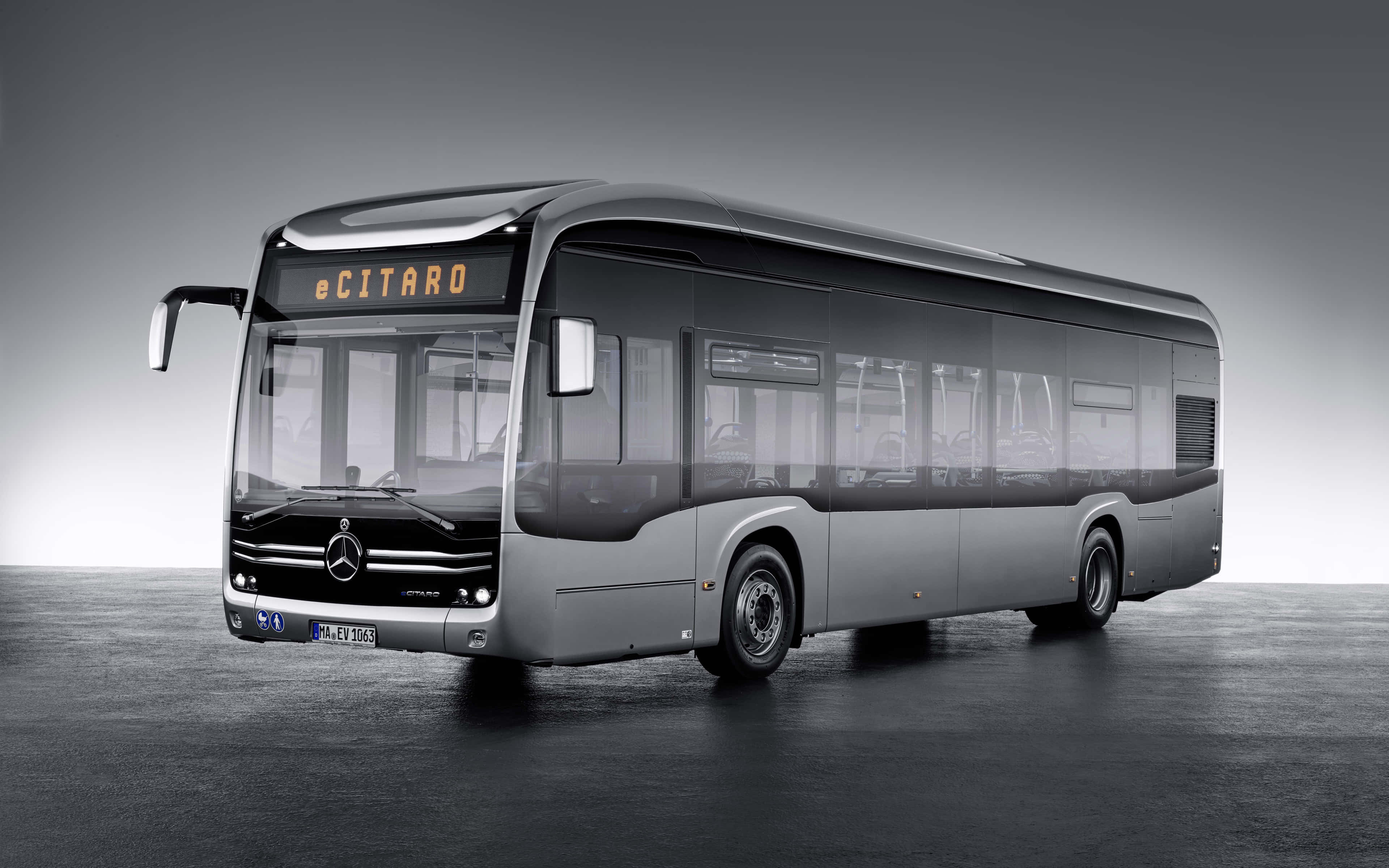Bus 桌布 壁紙 — 一輛時尚的銀色 Mercedes-Benz eCitaro 巴士，配備橙色目的地顯示屏，矗立在簡約的灰色工作室地板上。