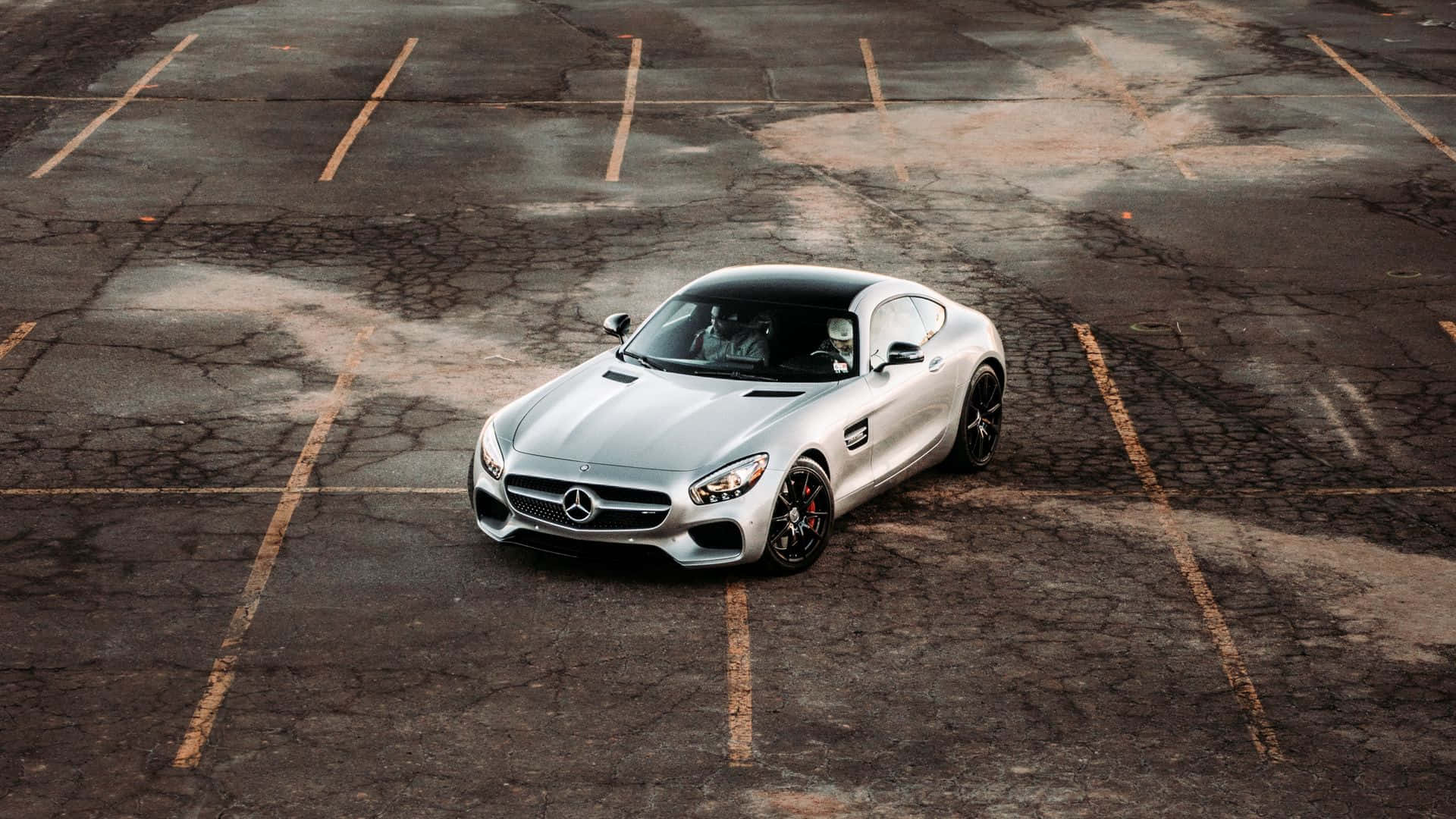 桌面 4K 桌布 壁紙 — 一輛時尚的銀色 Mercedes-AMG GT 跑車停放在一個有裂縫的瀝青停車場，地上有褪色的黃線。
