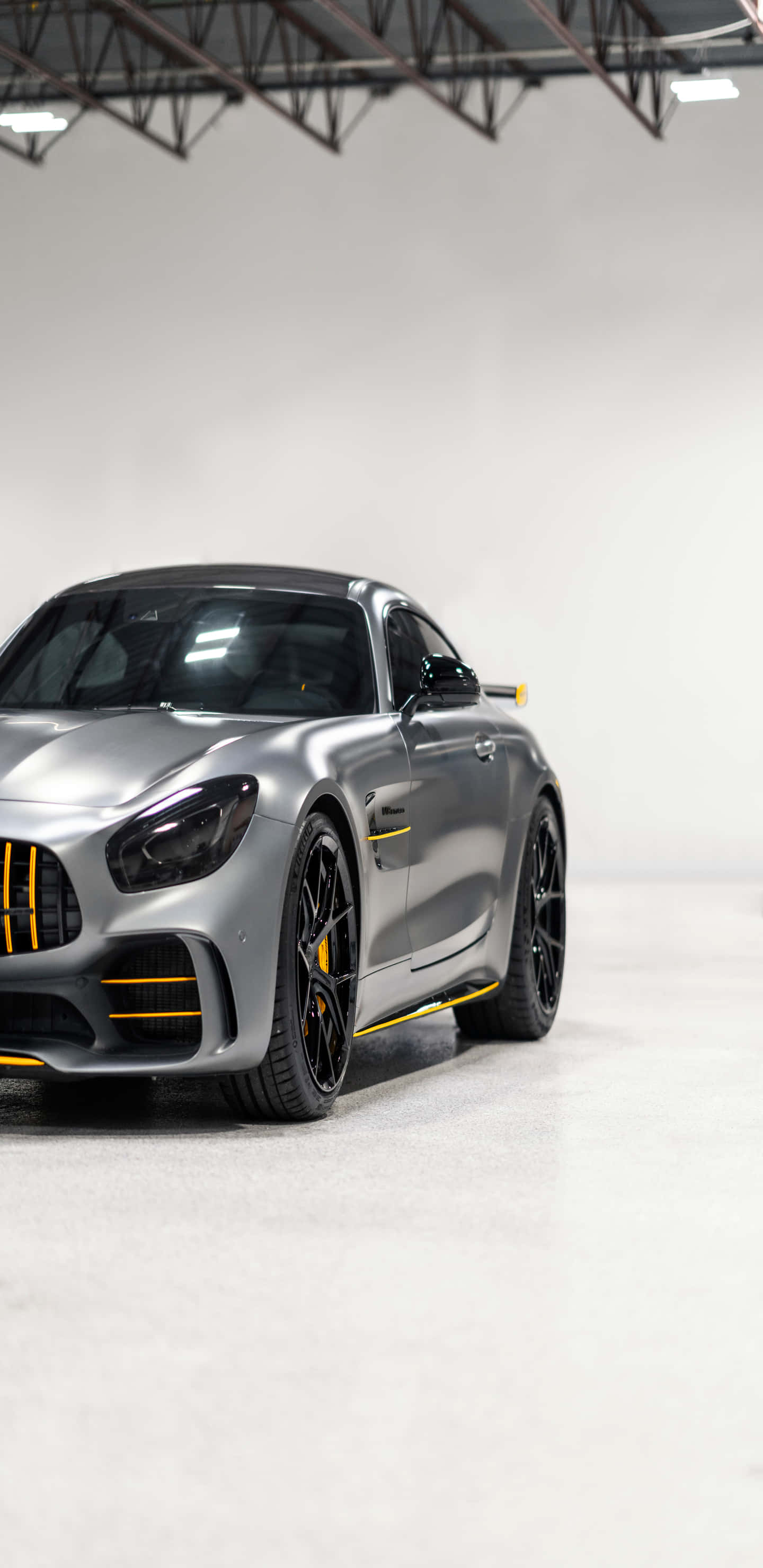 cars 桌布 壁紙 — 一輛時尚的銀色 Mercedes-AMG GT R 跑車帶有黃色點綴，停在工業照明下的簡約白色車庫中。