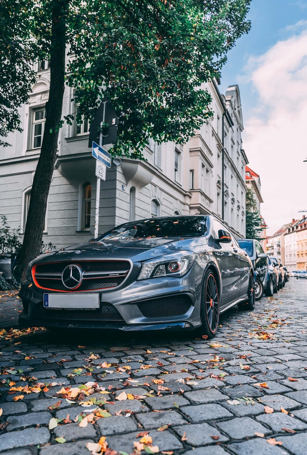 Mercedes 桌布 壁紙 — 一輛時尚的銀色 Mercedes-AMG CLA45 停泊在鋪滿秋葉的鵝卵石街道上，天空部分多雲。