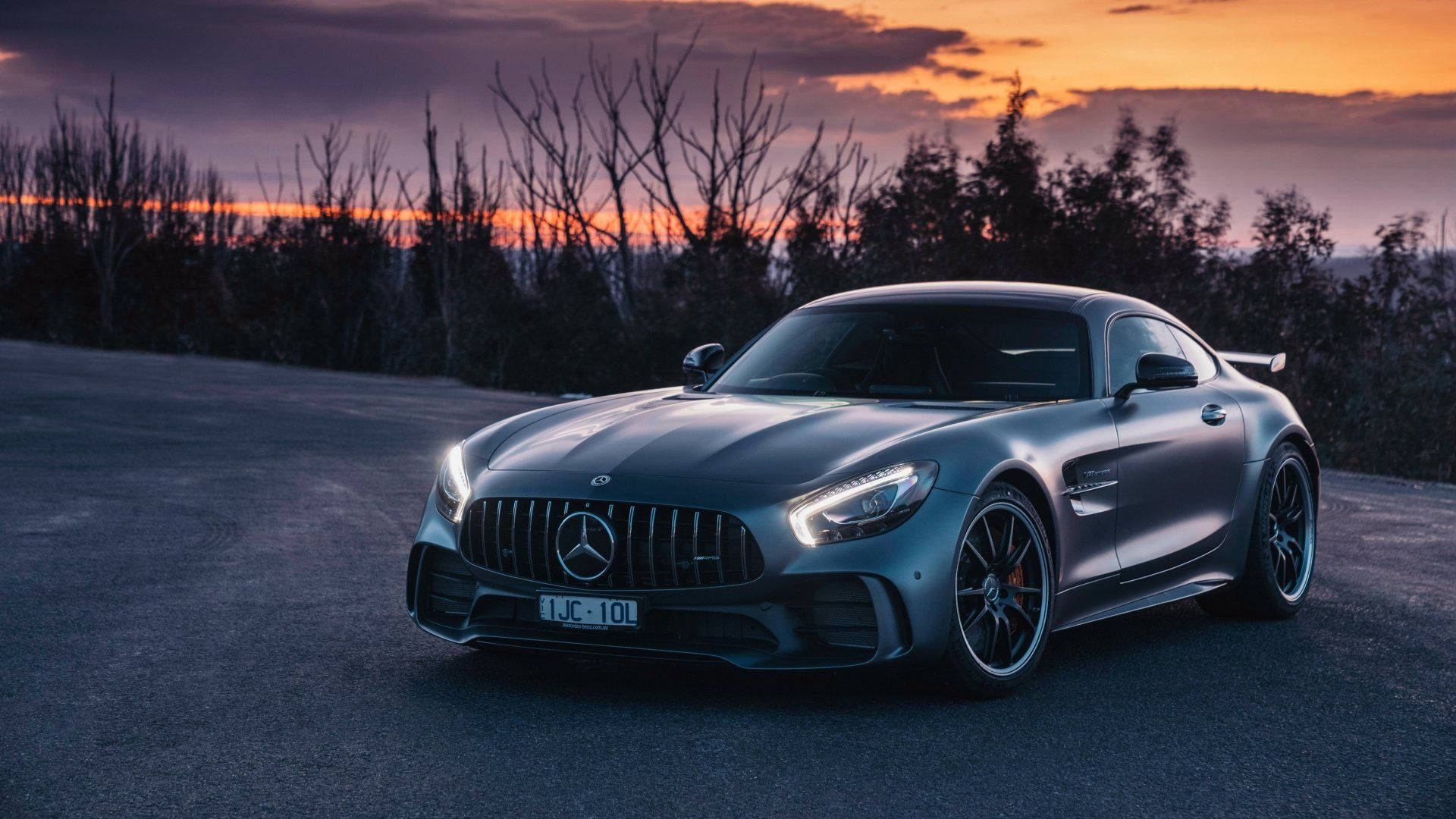 Gtr 桌布 壁紙 — 一輛時尚的銀色 Mercedes-AMG GT 停泊在日落時分的道路上，背景是光禿禿的樹木和橙色的天空。
