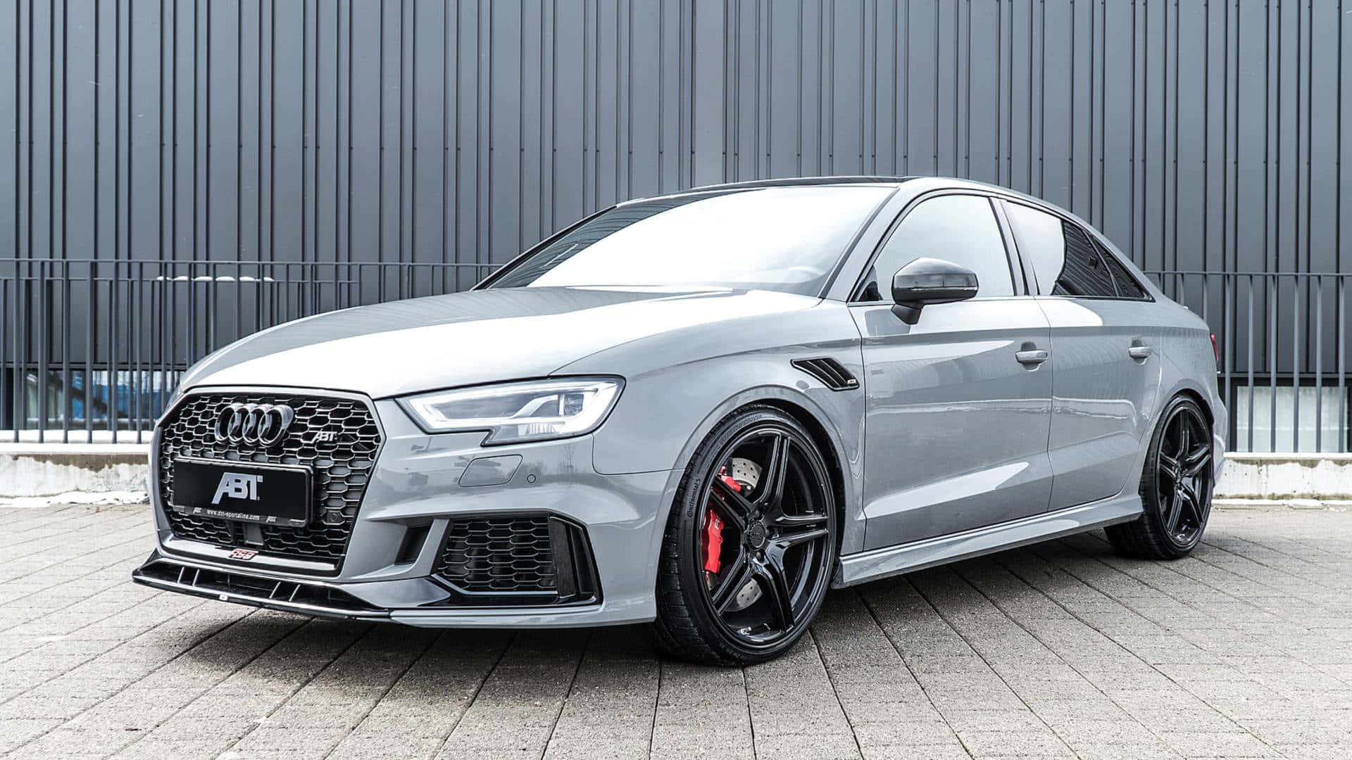 Sedan 桌布 壁紙 — 一輛時尚的銀色ABT改裝奧迪RS5運動轎車，停放在鋪砌路面上，背景是灰色波紋金屬牆。
