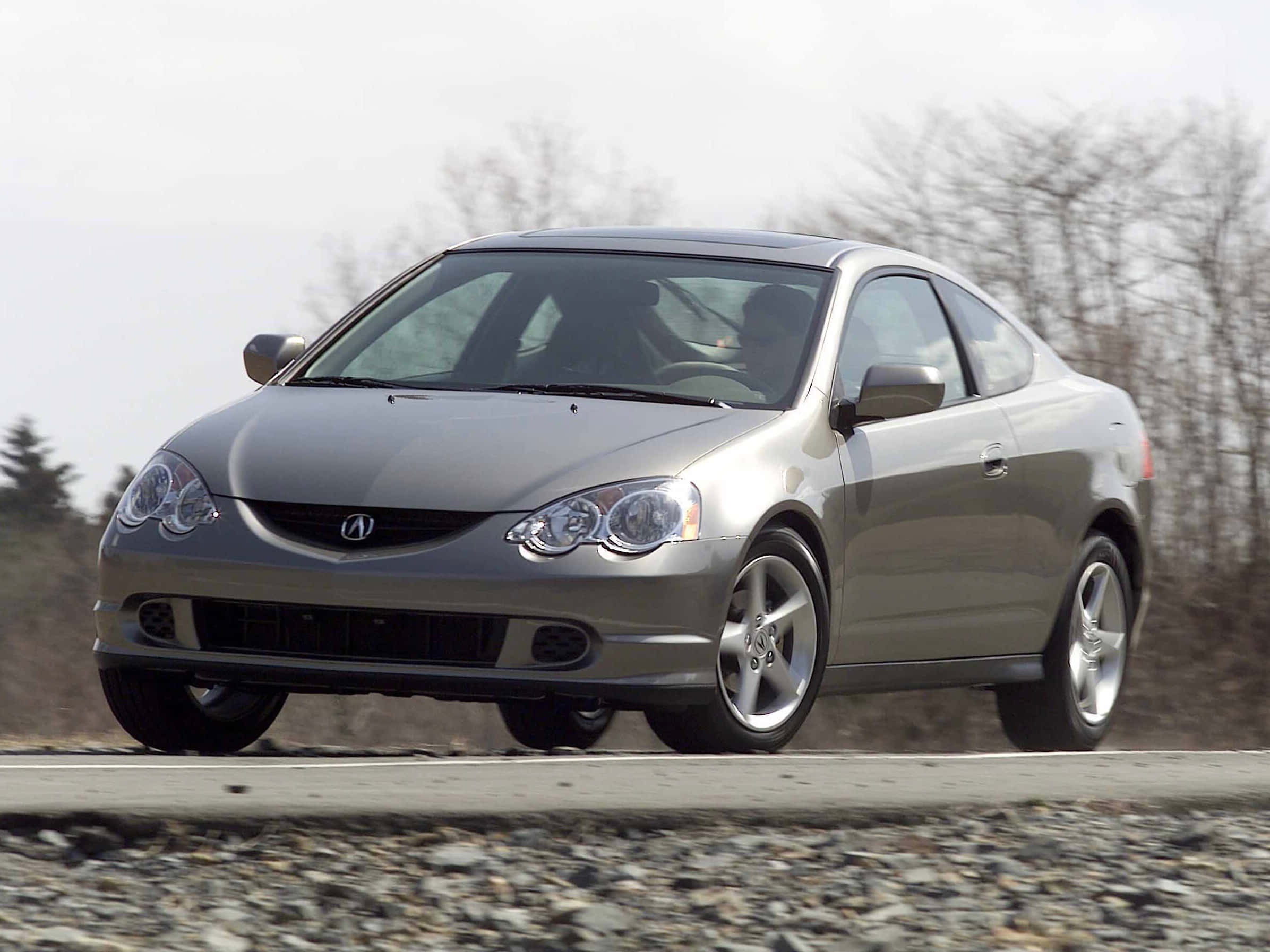Acura Rsx 桌布 壁紙 — 一輛時尚的銀色Acura TSX雙門轎跑車行駛在碎石路上，背景是光禿禿的樹木，天空多雲。