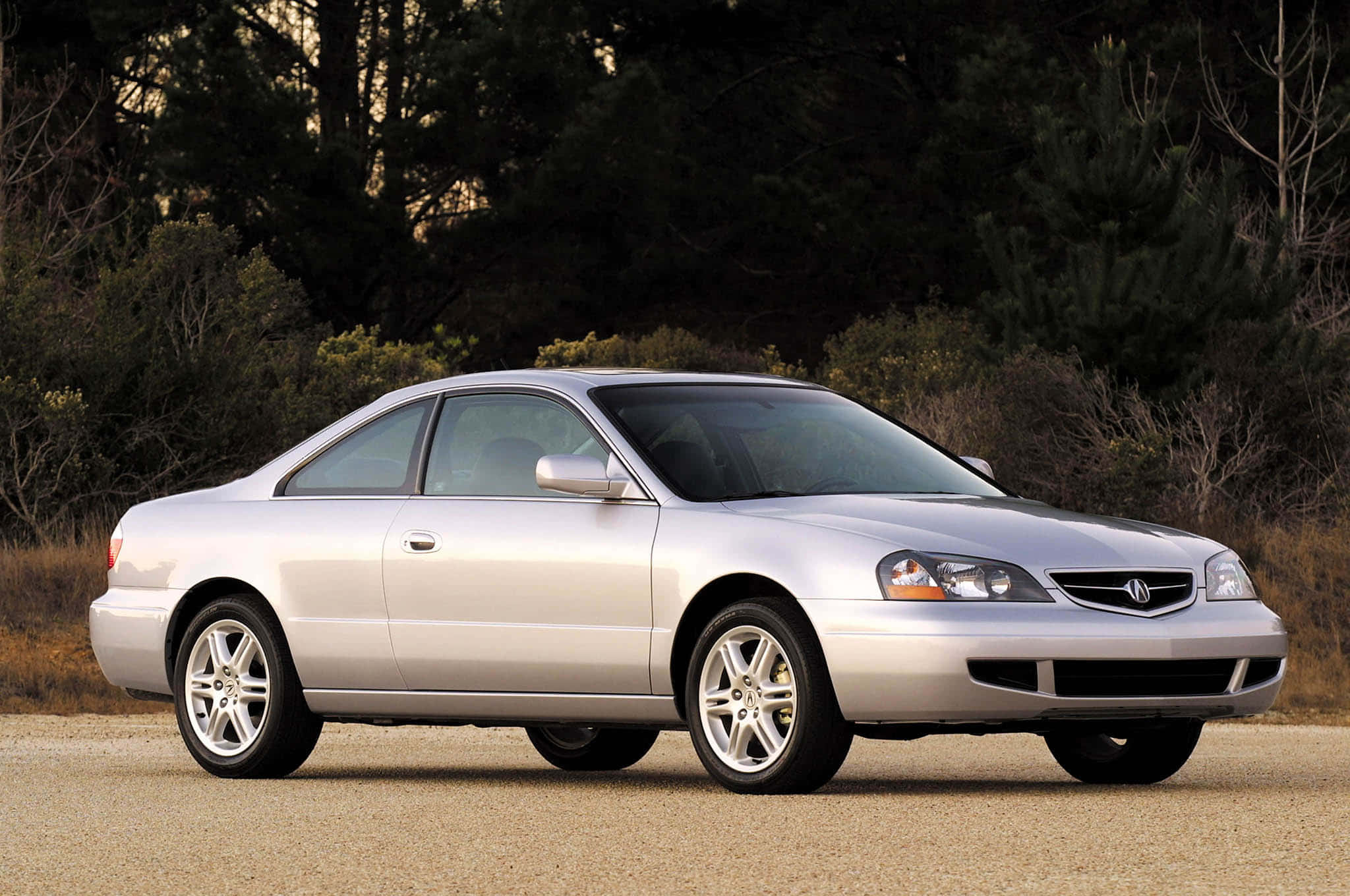 Acura 桌布 壁紙 — 一輛時尚的銀色Acura轎跑車停在碎石上，背景有樹木和灌木，在柔和日光下。