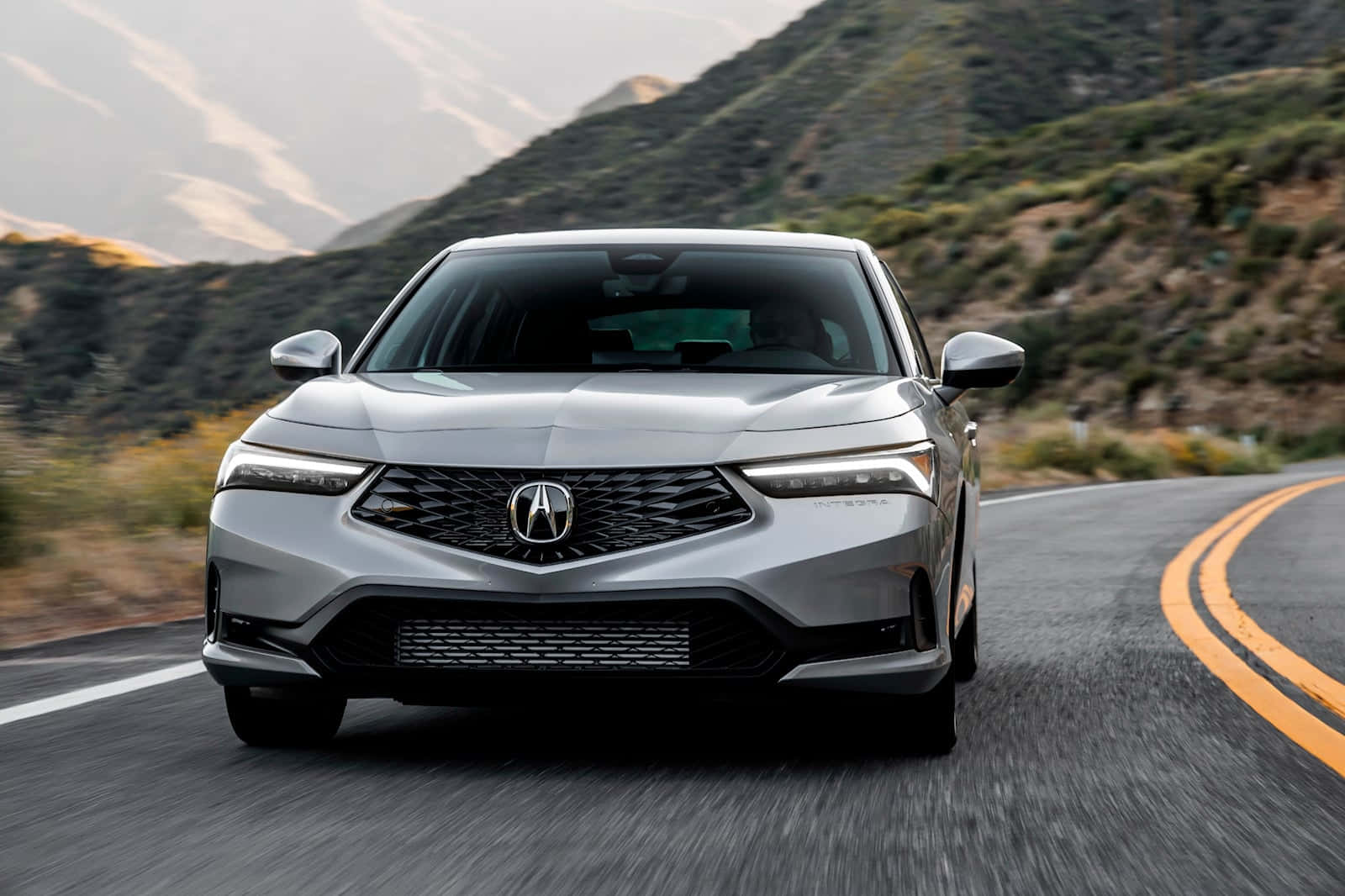 Acura Integra 桌布 壁紙 — 一輛時尚的銀色Acura轎車沿著蜿蜒的山路疾馳，帶有模糊的動感和金色的路邊標記。