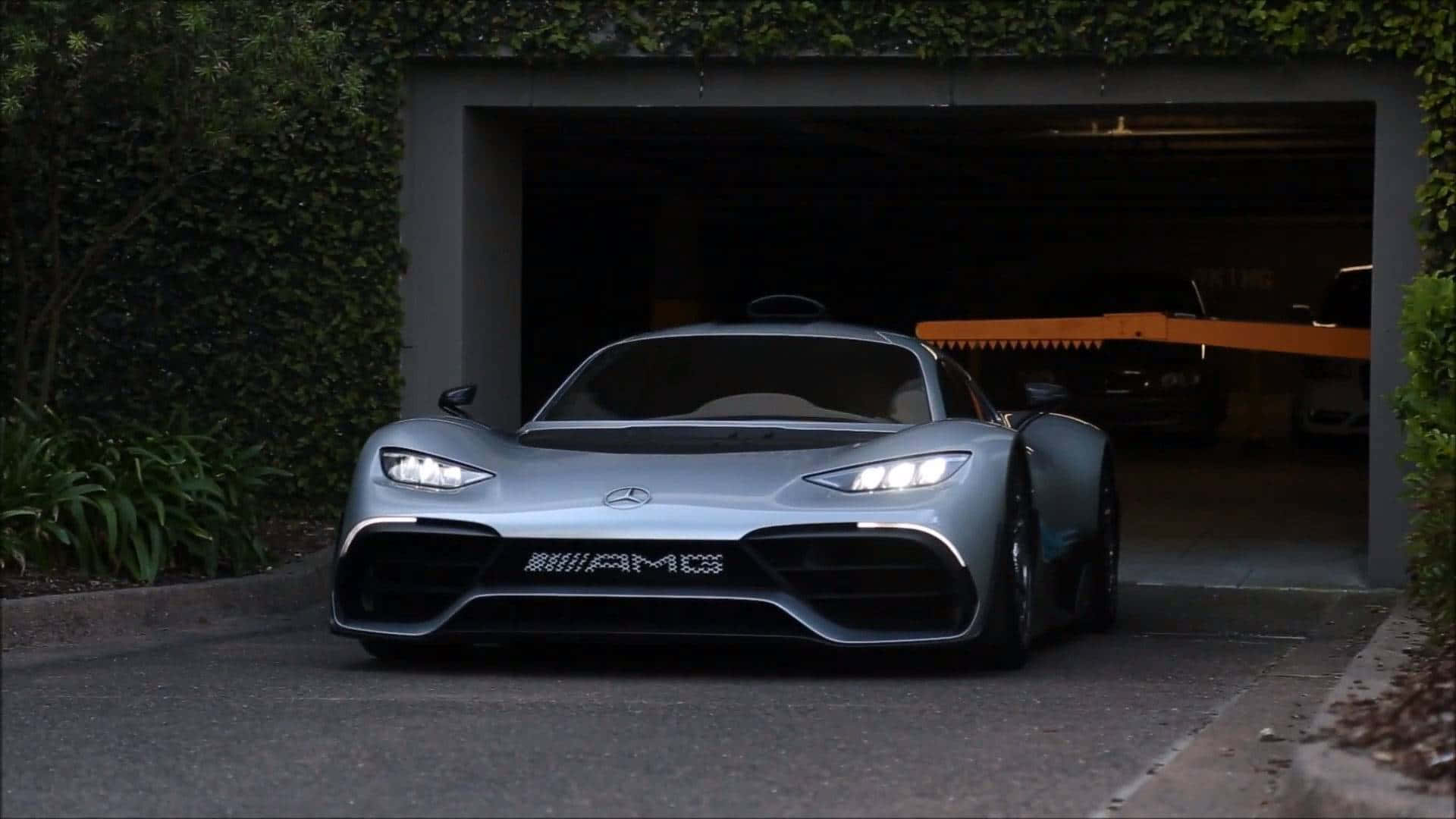 Mercedes 桌布 壁紙 — 一輛時尚的銀色AMG跑車，配備發光頭燈，從被茂密綠植環繞的現代車庫中駛出。