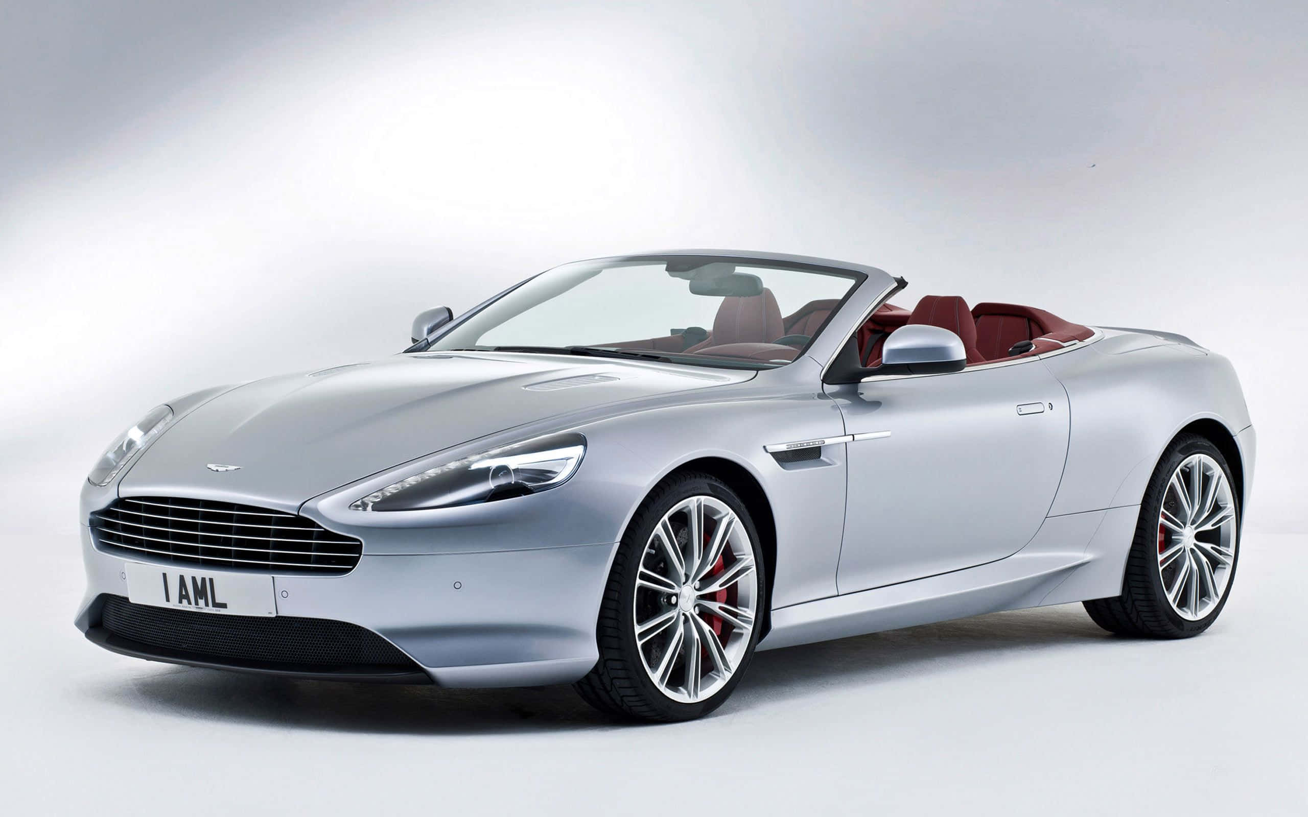 Aston Martin Db9 桌布 壁紙 — 一輛時尚的銀色Aston Martin DB9敞篷車，配備紅色內裝和鍍鉻輪圈，在明亮的白色工作室背景前擺拍。