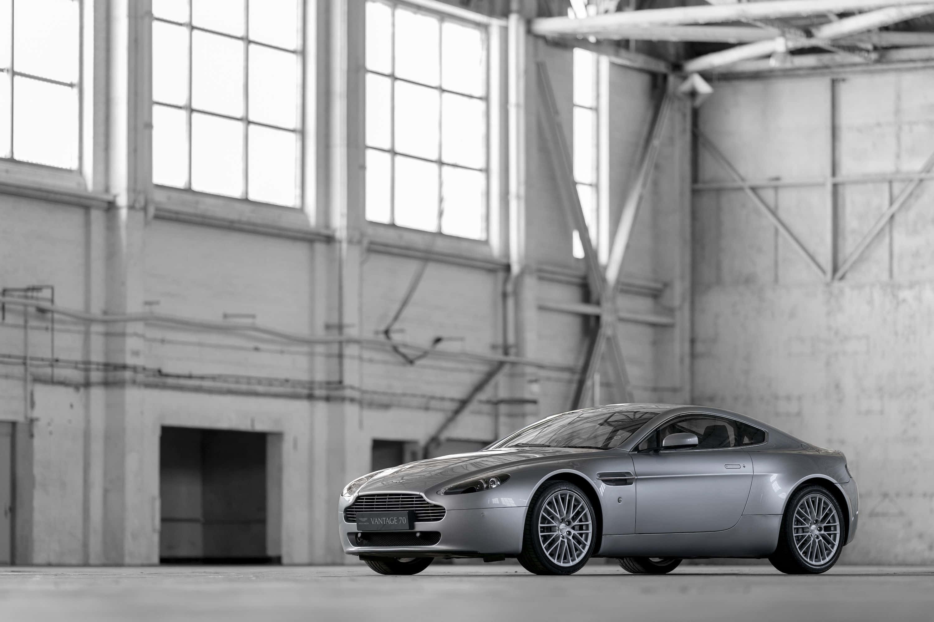 Aston Martin V12 Vantage 桌布 壁紙 — 一輛時尚的銀色Aston Martin Vanquish跑車停放在寬敞的高窗工業倉庫內。