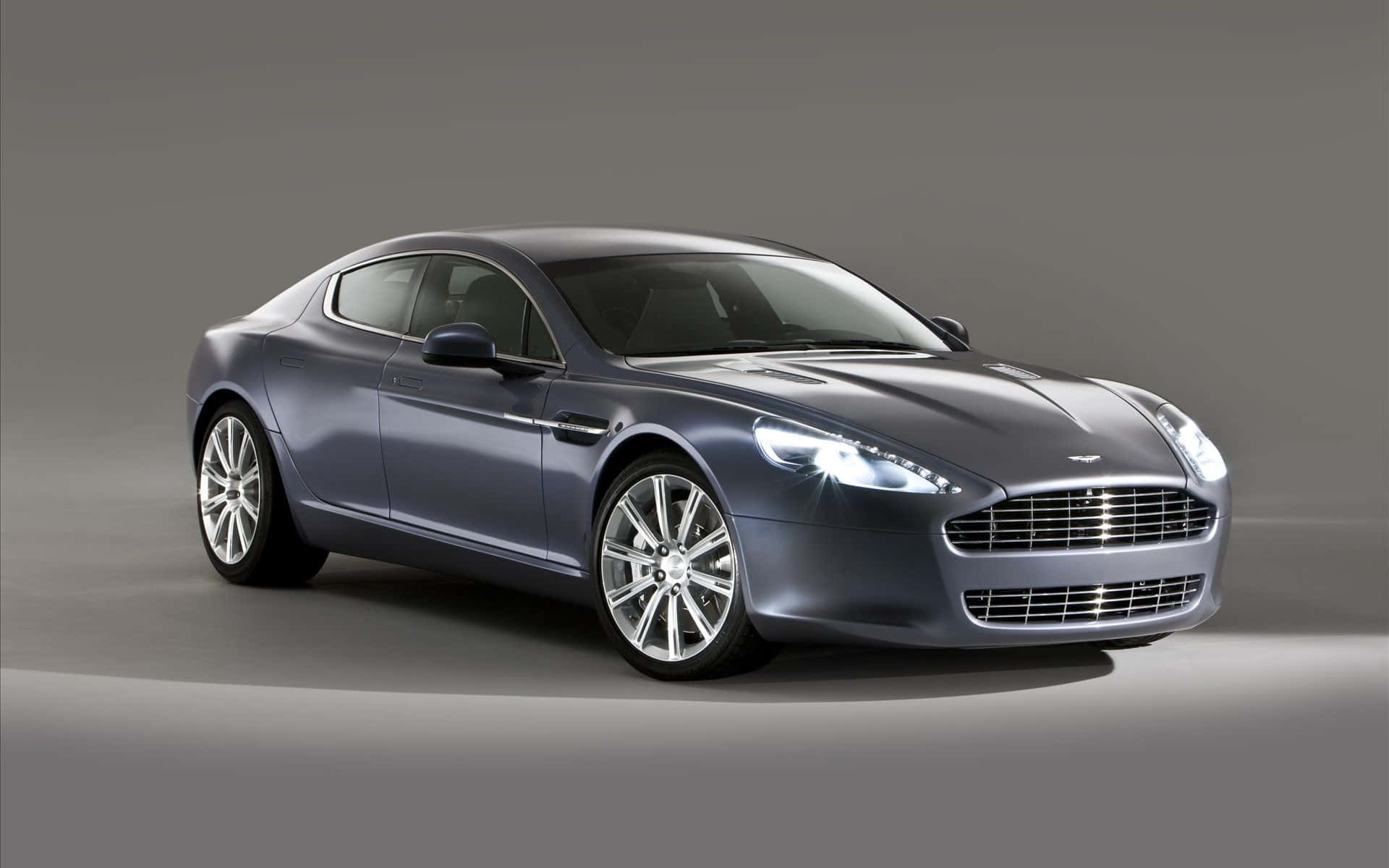 Aston Martin Rapide S 桌布 壁紙 — 一輛時尚的銀色Aston Martin跑車在工作室燈光下閃閃發光，背景為簡約灰色。