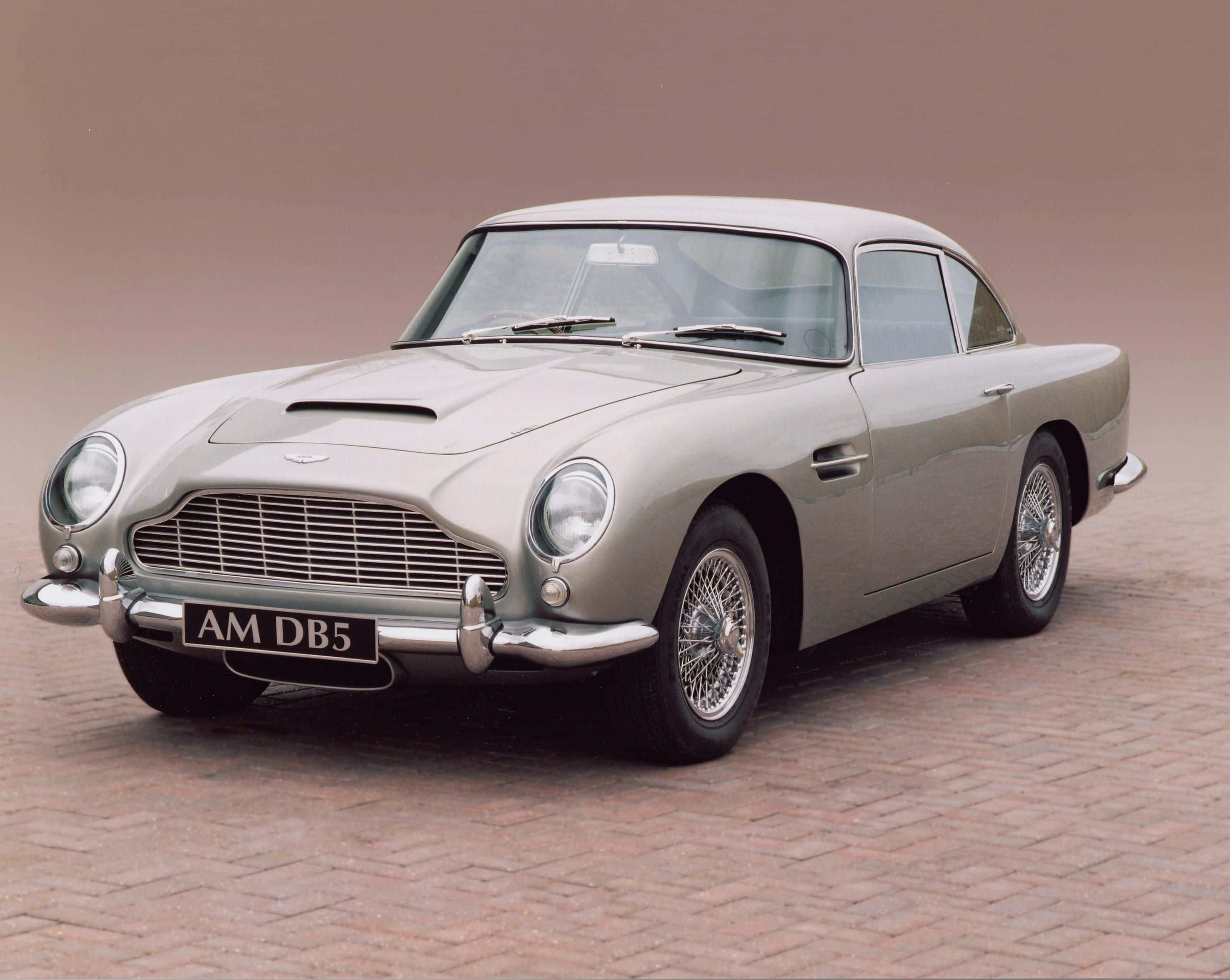 Aston Martin Db5 桌布 壁紙 — 一輛時尚的銀色Aston Martin DB5經典汽車停放在磚砌路面上，柔和的工作室燈光下。