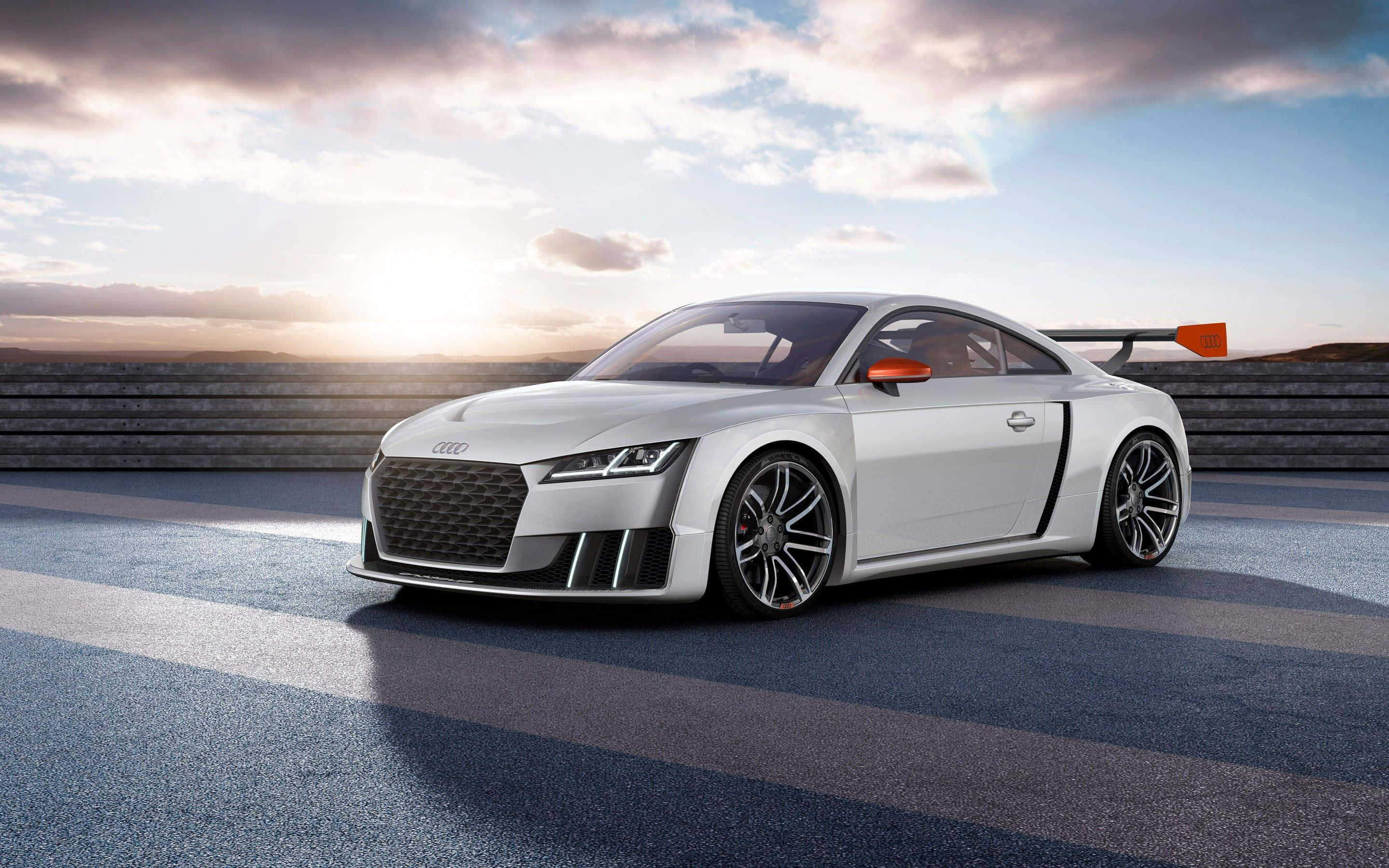 Audi Tt 桌布 壁紙 — 一輛時尚的銀色Audi TT賽車帶有橙色點綴，在日落時分停在賽道上，投下長長的影子。