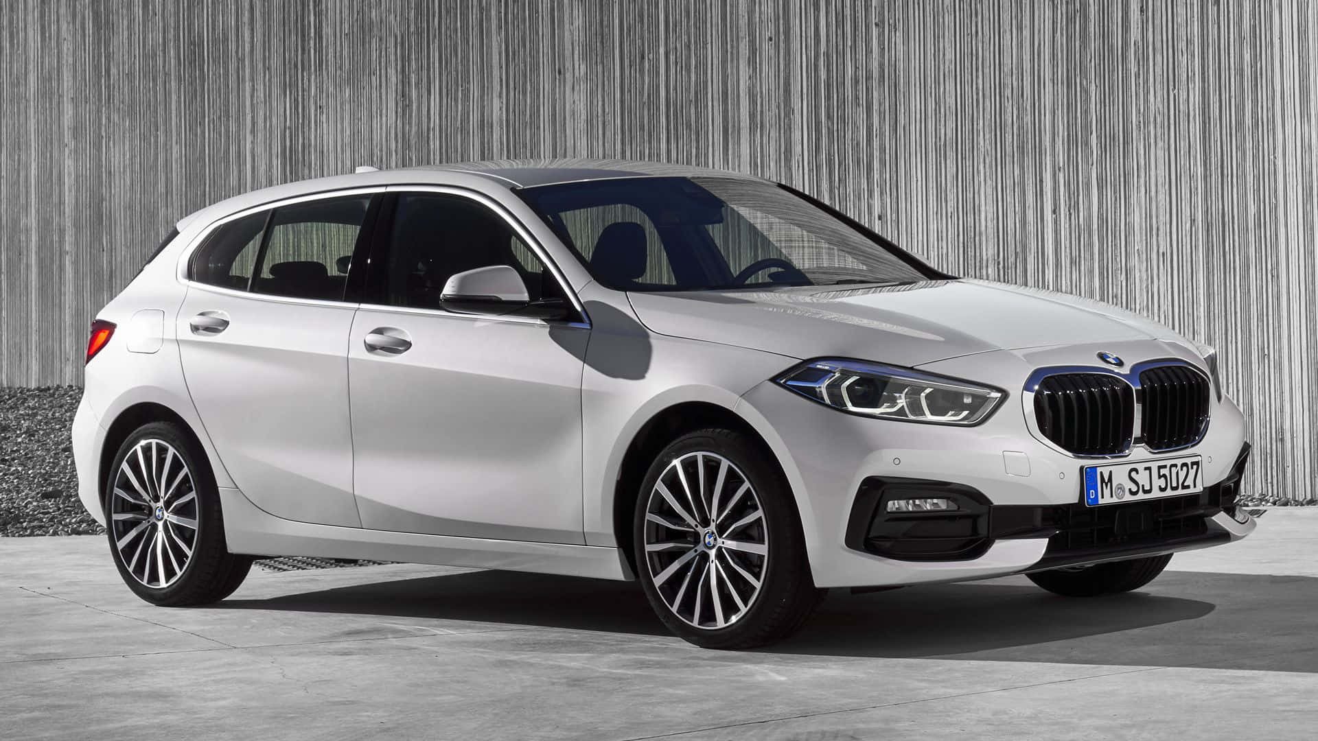 Bmw 1 Series 桌布 壁紙 — 一輛時尚的銀色BMW 1系列掀背車在明亮的日光下停靠在有紋理的灰色牆壁旁。