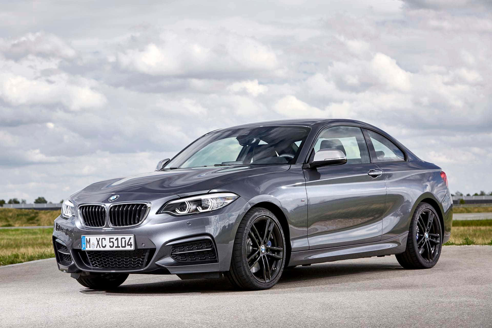Bmw 2 Series 桌布 壁紙 — 一輛時尚的銀色BMW 2系列轎跑車停在瀝青路上，天空多雲，背景是草地田野。