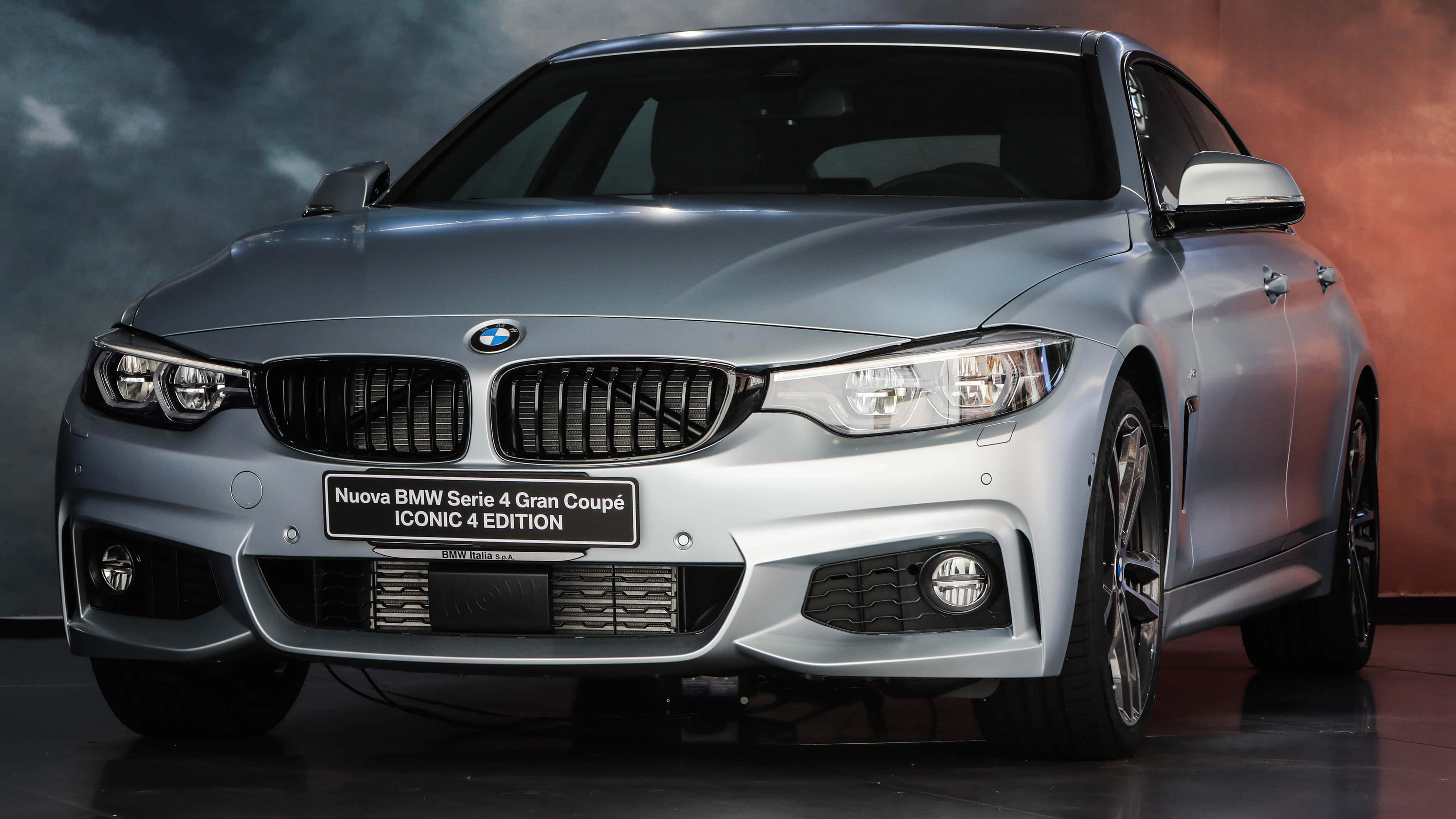 Bmw 440i 桌布 壁紙 — 一輛時尚的銀色BMW 4系列Gran Coupé Iconic Edition在攝影棚燈光下，以戲劇性的煙霧漸變背景閃耀光芒。