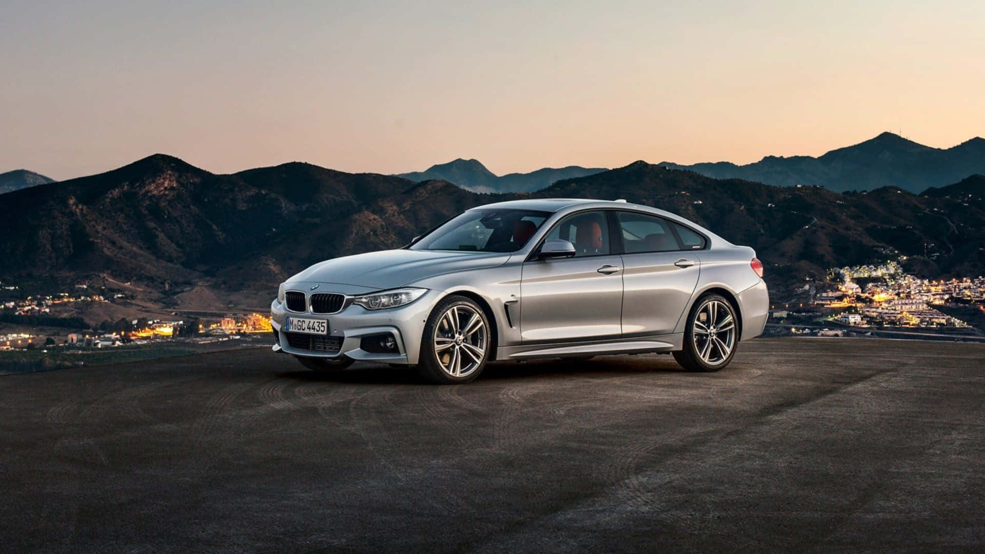 Bmw 4 Series 桌布 壁紙 — 一輛時尚的銀色BMW 4系列轎跑車在黃昏時停在山頂上，下方是山脈和燈火通明的城鎮。