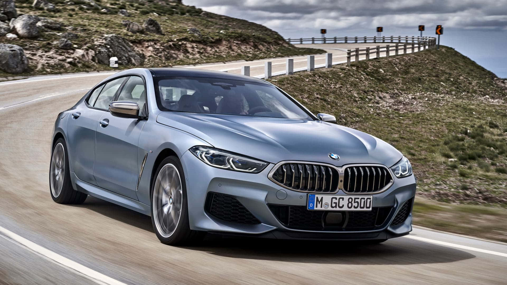 BMW 動圖 桌布 壁紙 — 一輛時尚的銀色BMW 8系列轎跑車在陰天下行駛在蜿蜒的山路上。