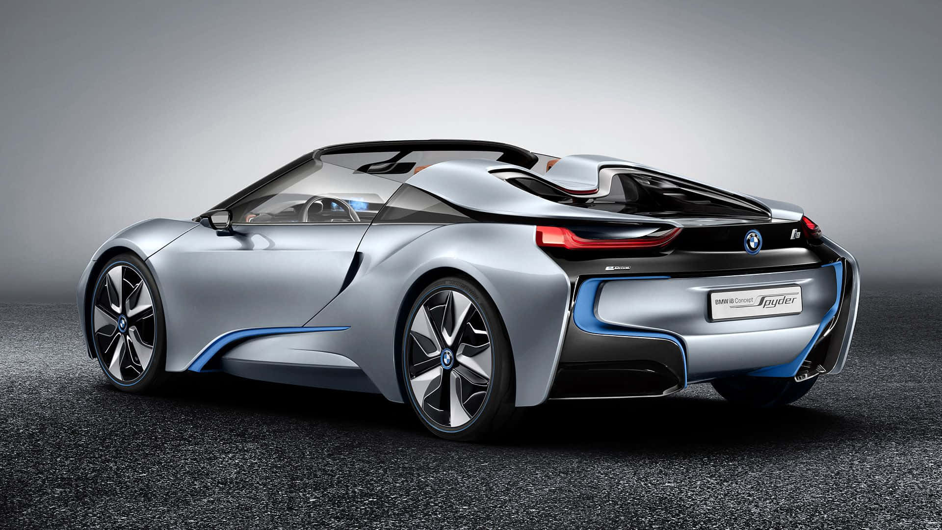 跑車 桌布 壁紙 — 一輛時尚的銀色BMW i8 Spyder概念車，帶有藍色飾條和紅色尾燈，從後方四分之三視角展示在深色紋理表面上，背景為漸變灰色。