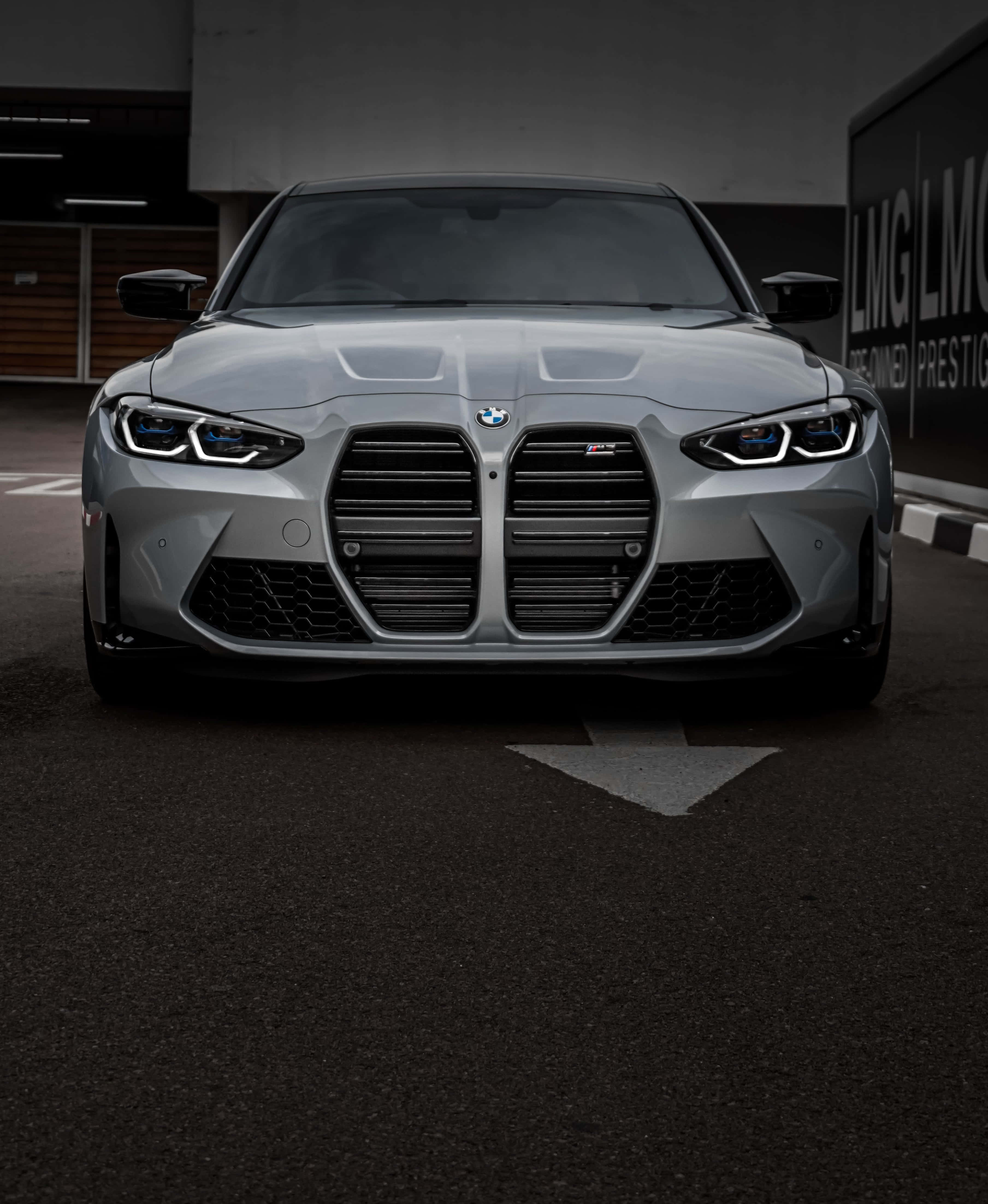 Best M Series 桌布 壁紙 — 一輛時尚的銀色BMW M3跑車，車頭燈閃爍，停泊在燈光昏暗的車庫中。
