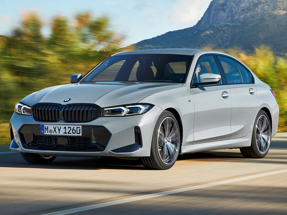 BMW 動圖 桌布 壁紙 — 一輛時尚的銀色BMW M3轎車在陽光明媚的山路上奔馳，背景是模糊的綠植和岩石山峰。