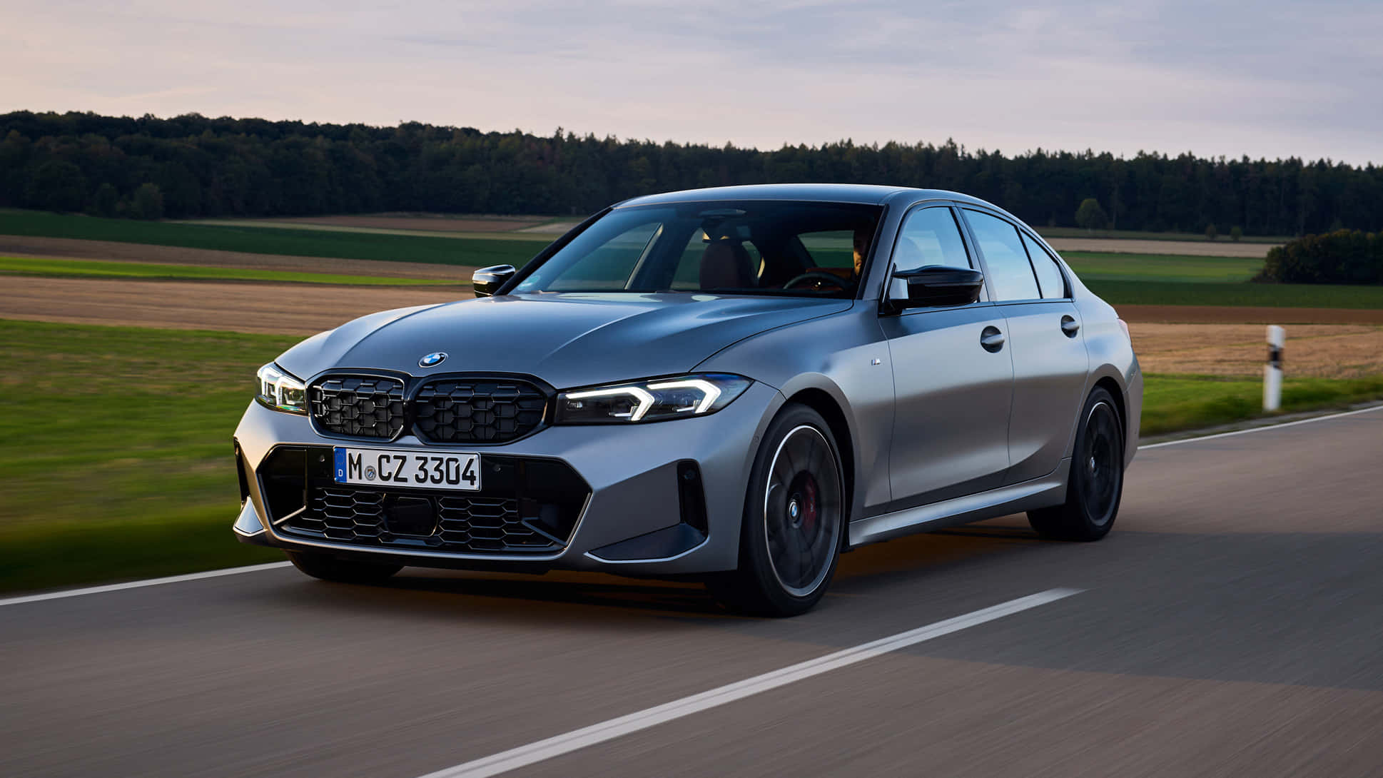 Bmw 3 Series 桌布 壁紙 — 一輛時尚的銀色BMW M3轎車在黃昏時分沿著鄉村道路疾馳，背景是模糊的田野和樹木。