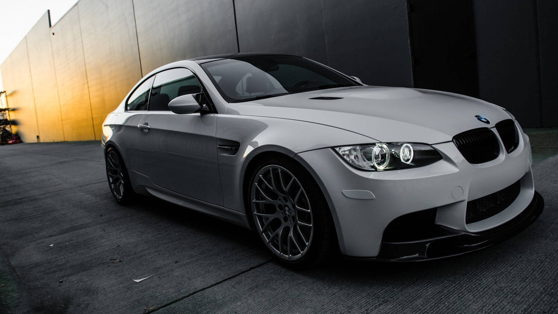 BMW 動圖 桌布 壁紙 — 一輛時尚的銀色BMW M3雙門跑車停在對比鮮明的黃黑牆前，沐浴在金色陽光下。