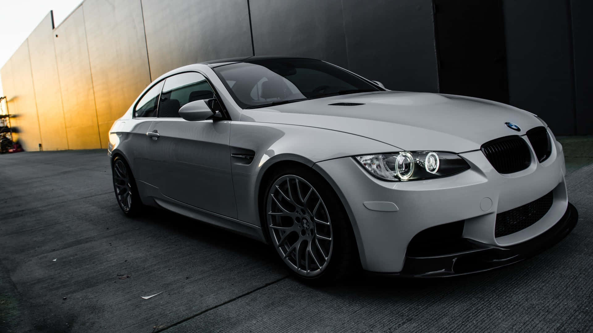 1920x1080 Bmw 桌布 壁紙 — 一輛時尚的銀色BMW M3雙門跑車停在對比鮮明的深色牆壁旁，沐浴在溫暖的黃金時刻光線中。