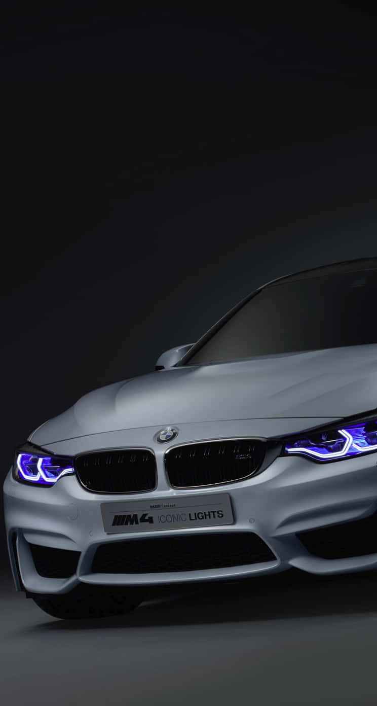 Bmw iPhone 桌布 壁紙 — 一輛時尚的銀色BMW M4配備發光的藍色頭燈，在黑暗的攝影棚環境中佔據主導地位。