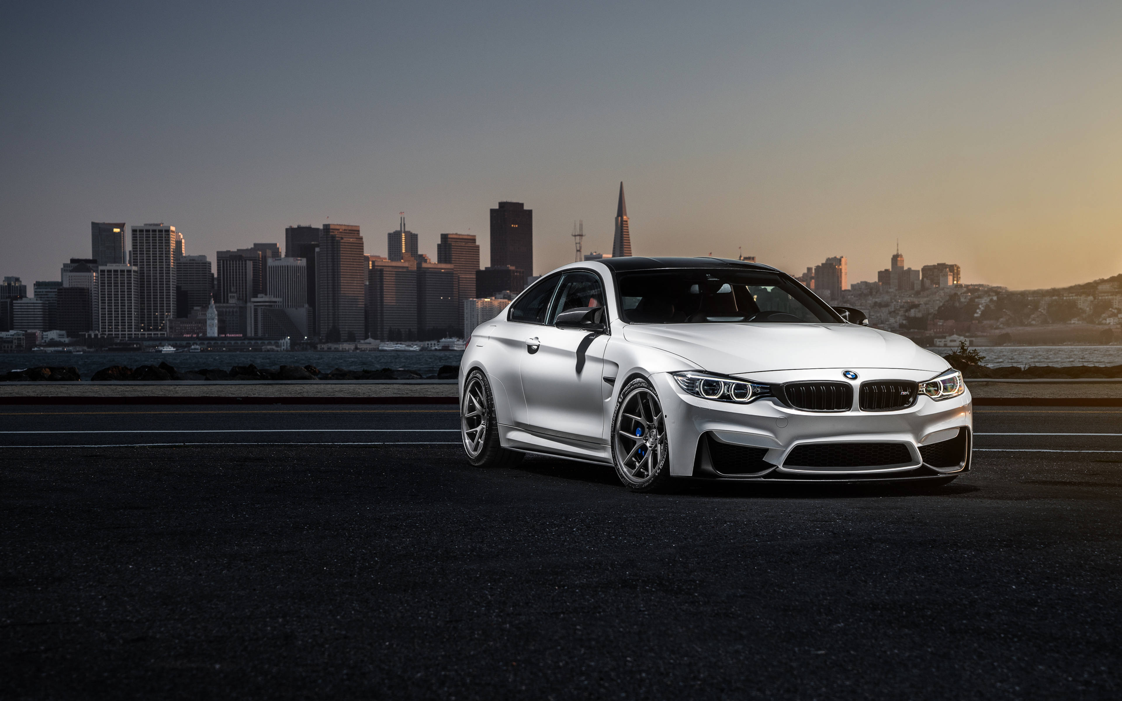 Bmw M Series 桌布 壁紙 — 一輛時尚的銀色BMW M4雙門轎跑車停在高速公路上，舊金山天際線在日落時分閃耀著光芒。