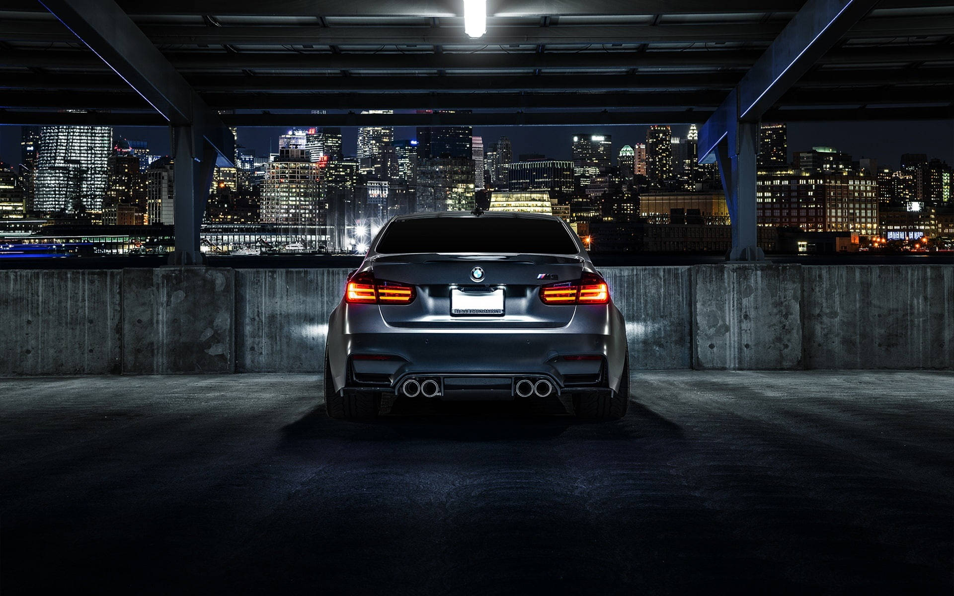 BMW 動圖 桌布 壁紙 — 一輛時尚的銀色BMW M5在夜間停泊在一個城市停車場，俯瞰著充滿活力的城市天際線。