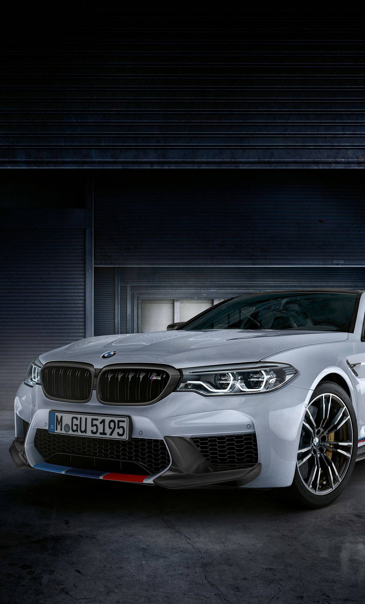X 桌布 壁紙 — 一輛時尚的銀色BMW M5跑車在昏暗的工業車庫中，在戲劇性的燈光下閃閃發光。