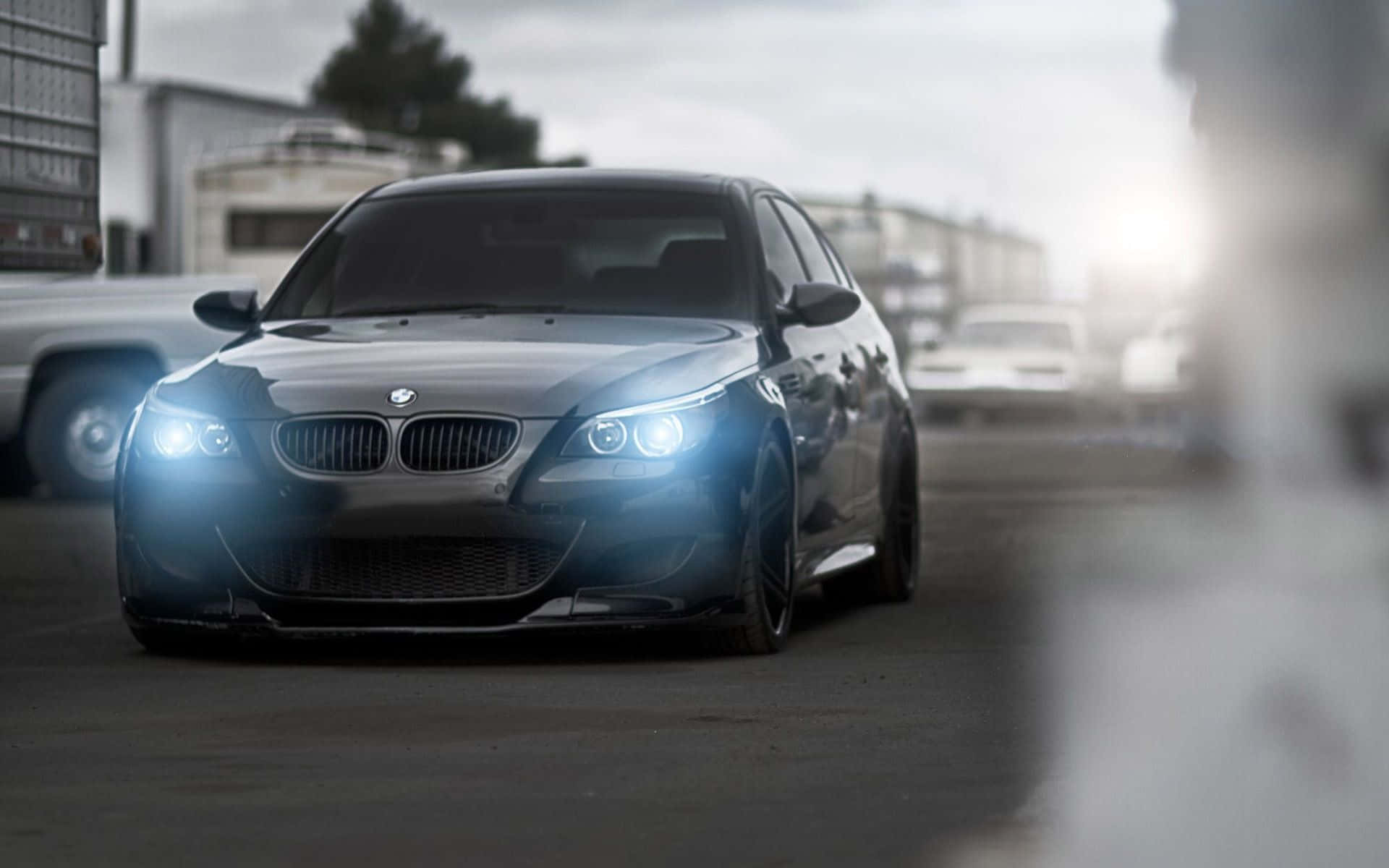 BMW 動圖 桌布 壁紙 — 一輛時尚的銀色BMW M5轎車，配備發光的車頭燈，在陰天籠罩下的骯髒城市街道上駛向鏡頭。