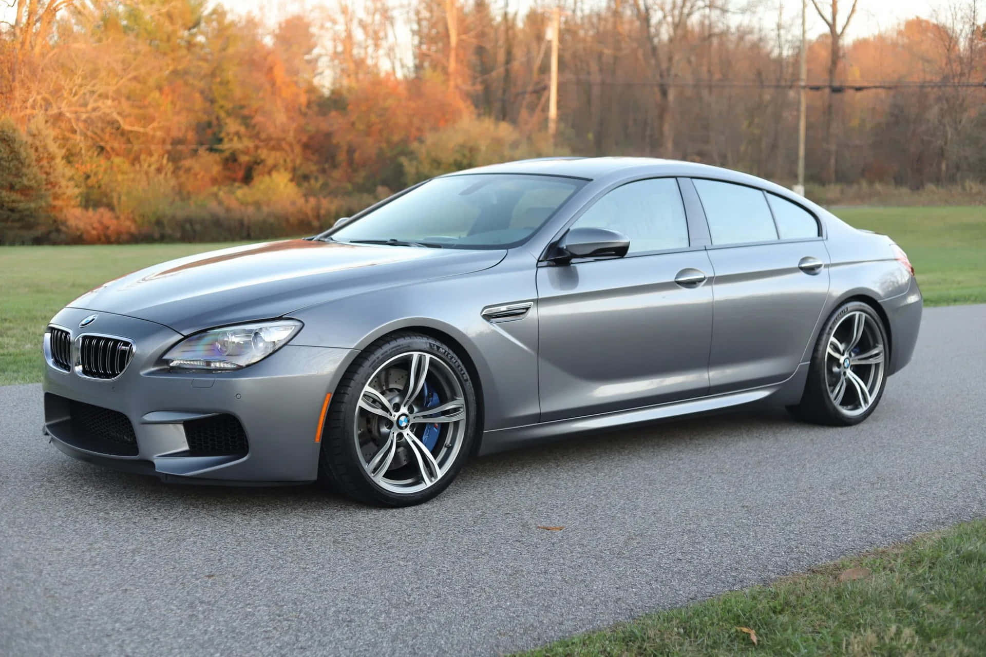 Bmw M6 桌布 壁紙 — 一輛時尚的銀色BMW M6跑車停在碎石路上，身後秋日樹木在溫暖光線中閃耀。