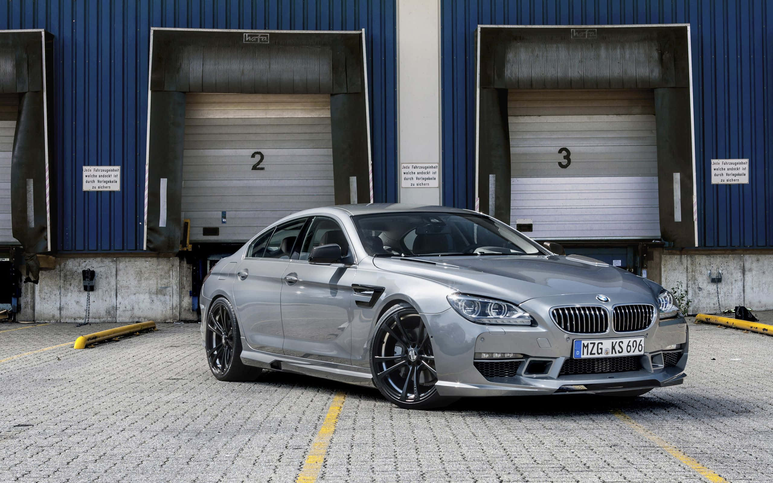 Bmw 6 Series 桌布 壁紙 — 一輛時尚的銀色BMW M6轎跑車停在工業藍色倉庫門前的鋪砌場地上。