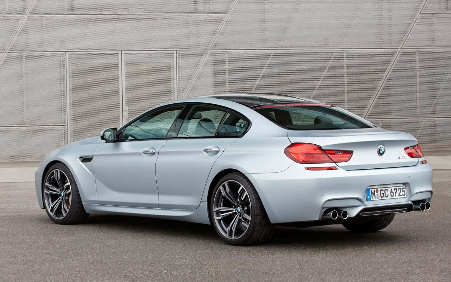 Bmw M6 桌布 壁紙 — 一輛時尚的銀色BMW M6轎跑車停泊在現代金屬網牆前，展示其運動型設計和雙排氣管。