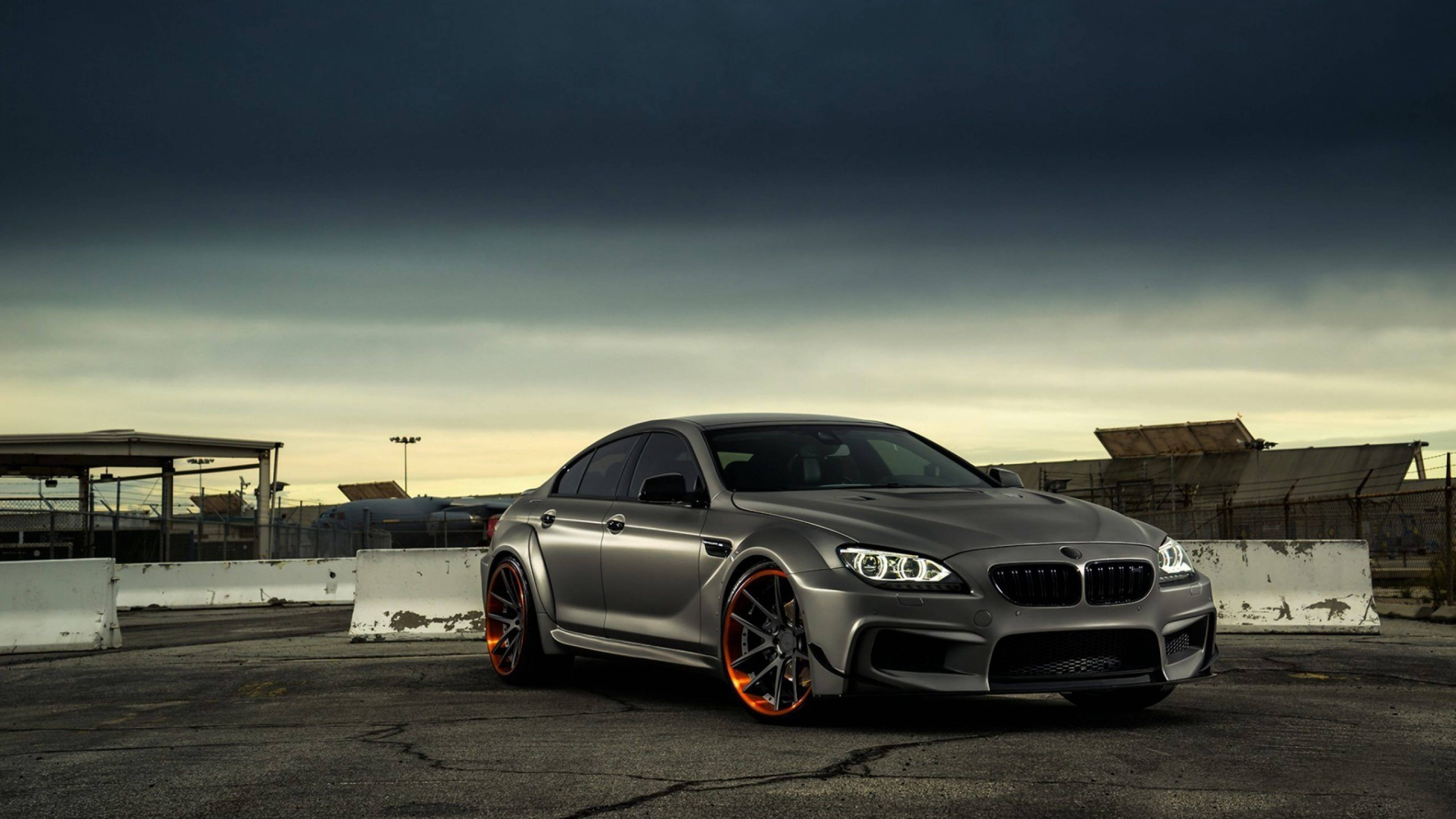 4K BMW 壁紙 桌布 壁紙 — 一輛時尚的銀色BMW M6配橙色輪圈，停在裂開的瀝青地上，背景是戲劇性的黃昏天空。