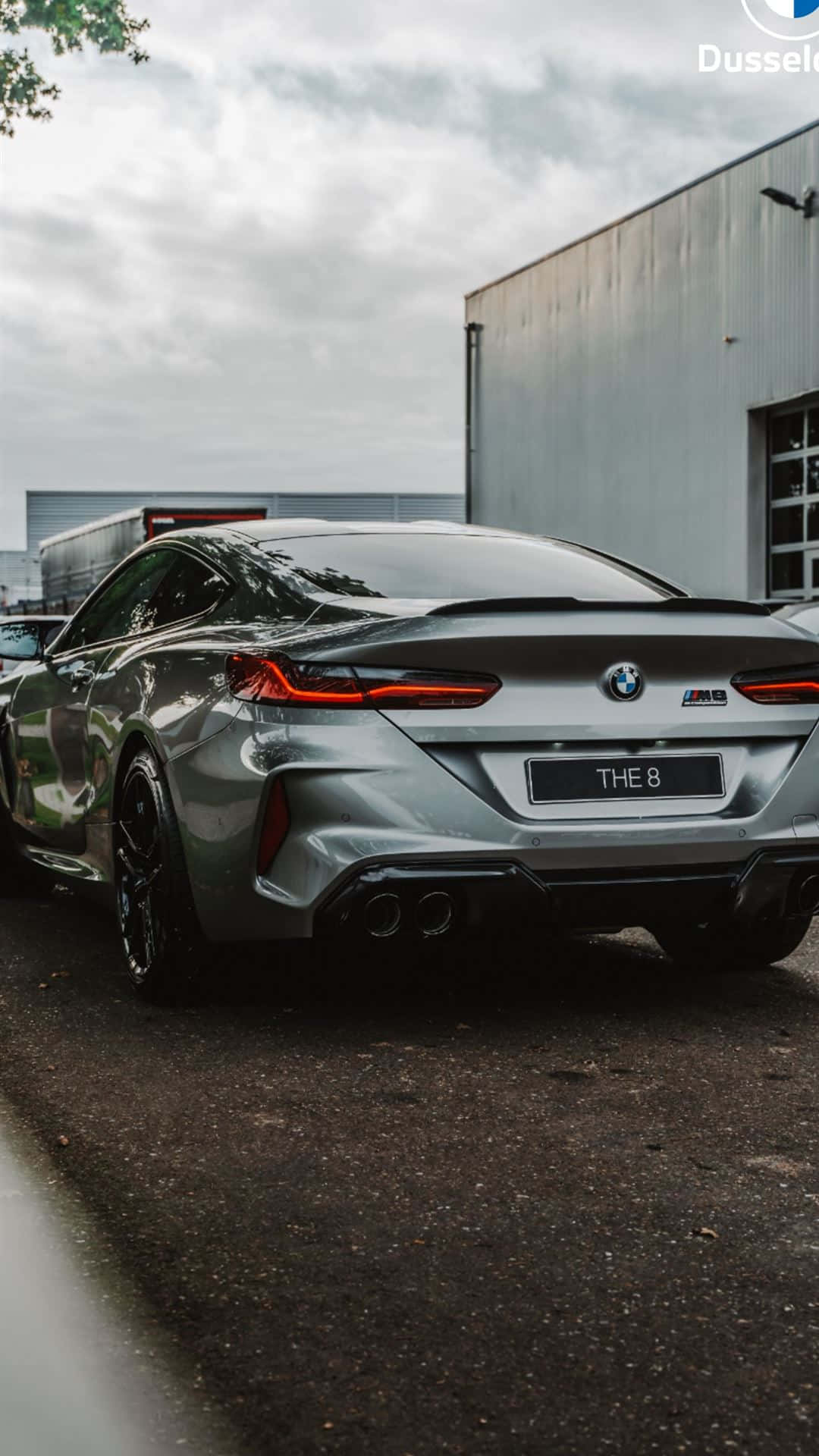 Bmw M8 4K 桌布 壁紙 — 一輛時尚的銀色BMW M8 Coupe停放在戶外，背景是陰天和工業建築。