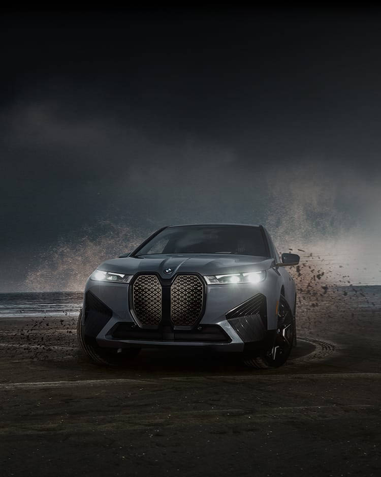 m 桌布 壁紙 — 一輛時尚的銀色BMW SUV在暴風雨的海灘上，亮著車頭燈駛過深色沙地。
