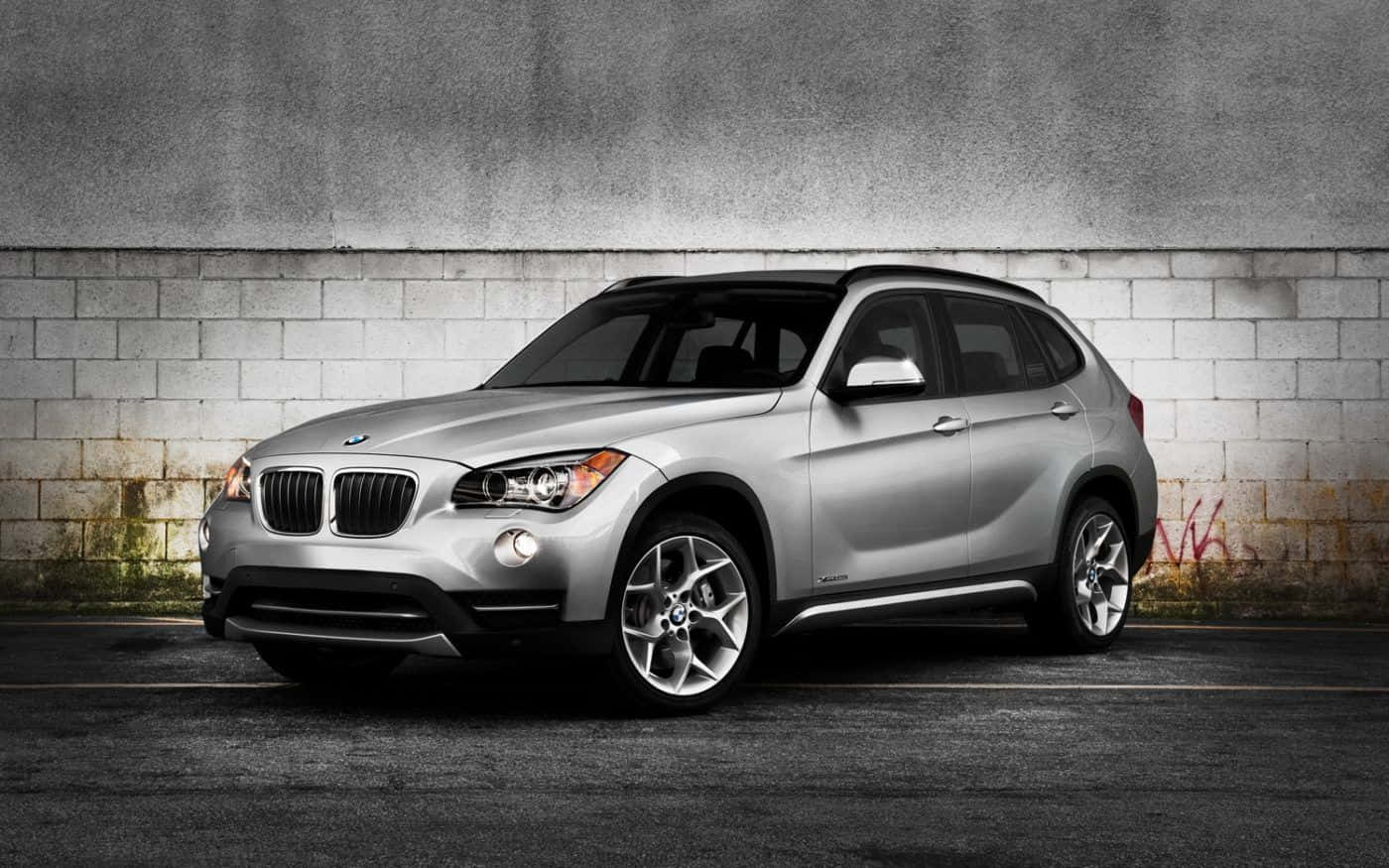 Bmw X1 桌布 壁紙 — 一輛時尚的銀色BMW X1 SUV停靠在經風化的混凝土牆旁，牆上有塗鴉。