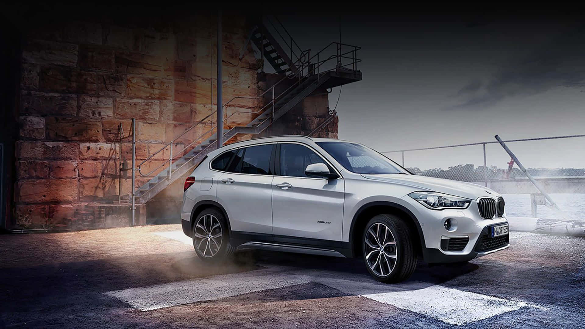 Bmw X1 桌布 壁紙 — 一輛時尚的銀色BMW X1 SUV停放在粗糙的工業碼頭上，蒸汽升騰，背後是風化的磚牆。