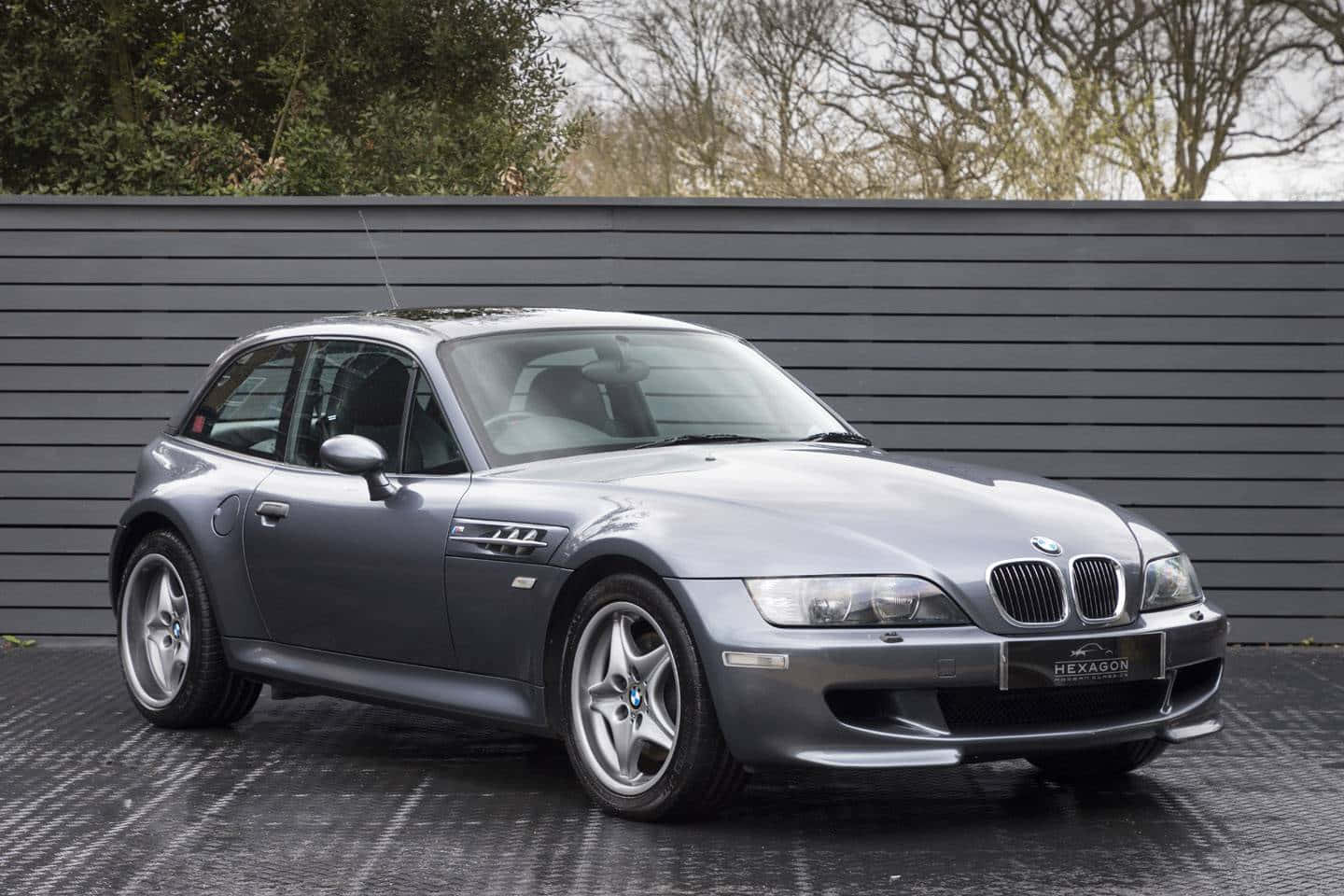 Bmw Z3 桌布 壁紙 — 一輛時尚的銀色BMW Z3敞篷跑車停放在濕漉漉的路面上，背景是深灰色條紋牆壁和光禿禿的樹木。