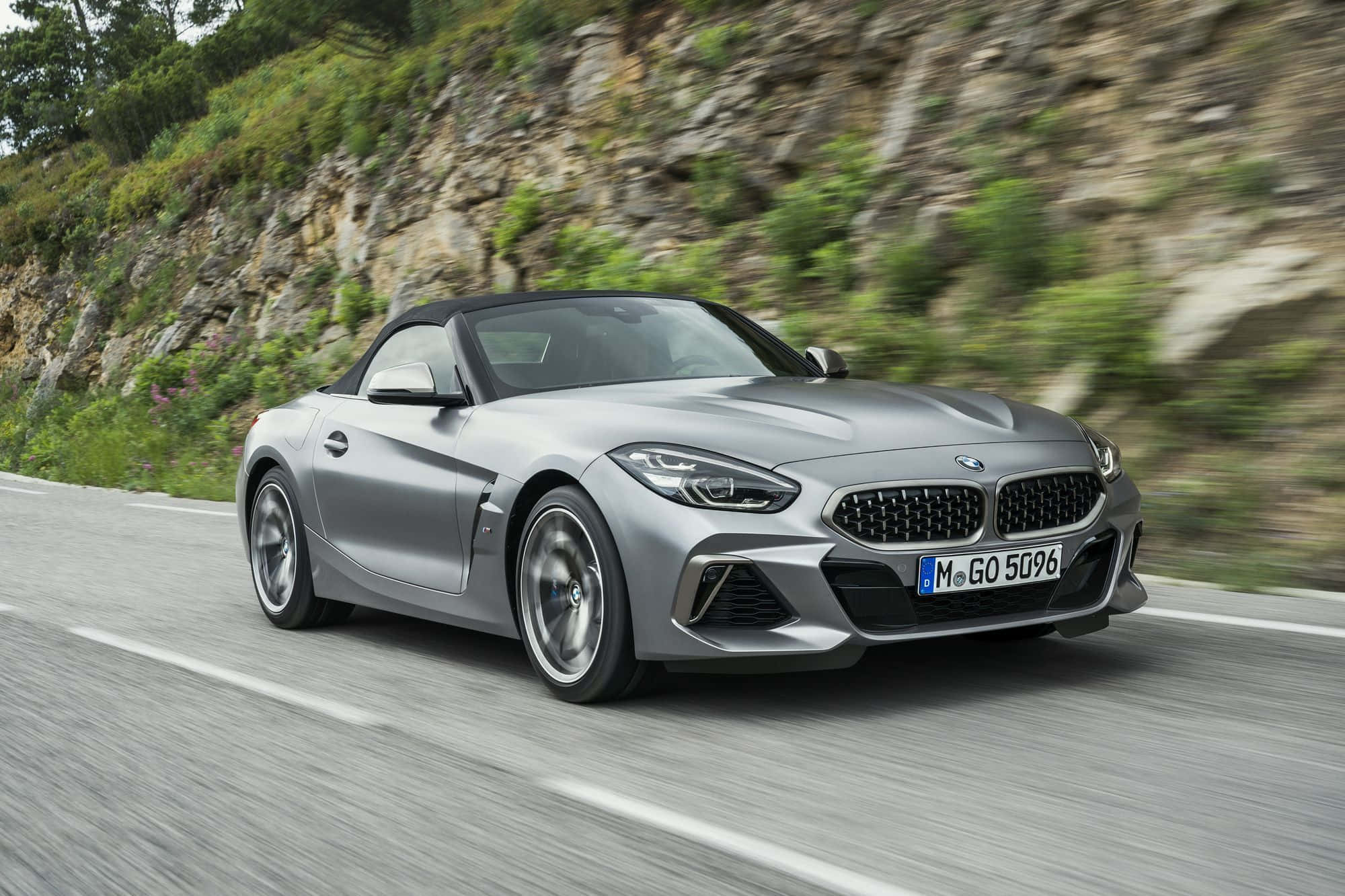Bmw Z4 桌布 壁紙 — 一輛時尚的銀色BMW Z4敞篷跑車在蜿蜒的山路上奔馳，背景是模糊的綠植和岩石峭壁。