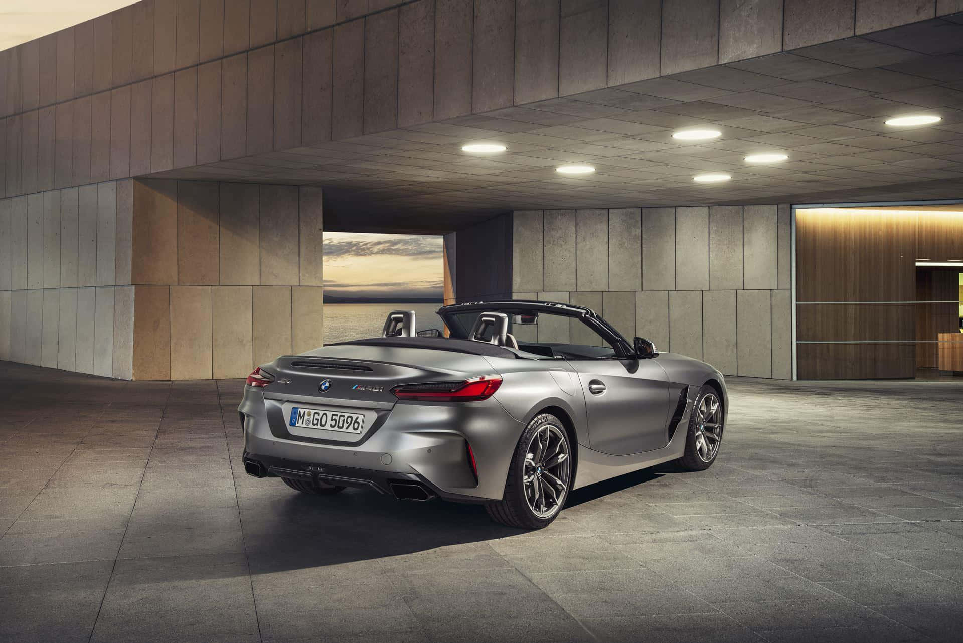 Bmw Z4 桌布 壁紙 — 一輛時尚的銀色BMW Z4敞篷車停放在現代混凝土結構下，夕陽光線從開口處照射進來。