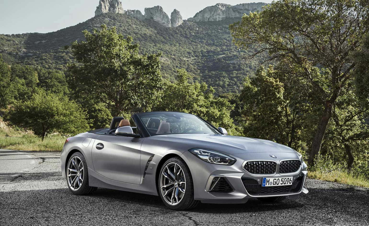 Bmw Z4 桌布 壁紙 — 一輛時尚的銀色BMW Z4敞篷車停在碎石路上，背景是茂密的綠樹和岩石山脈。