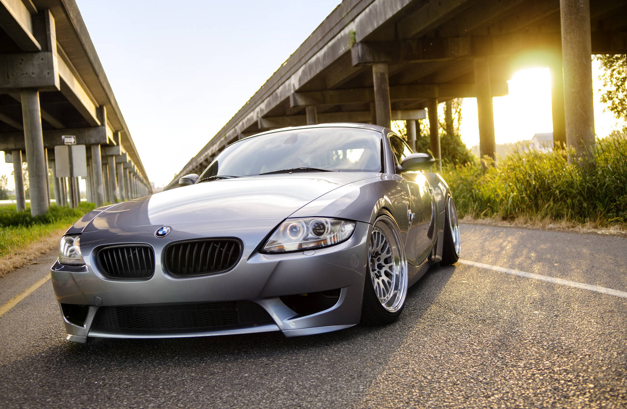 銀色 桌布 壁紙 — 一輛時尚的銀色BMW Z4跑車停在混凝土天橋下，金色夕陽在瀝青路上投下長長的影子。