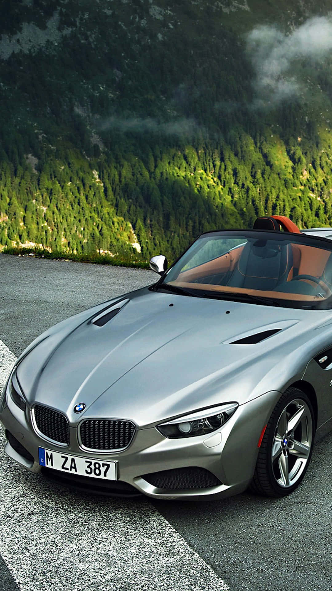Bmw Android 桌布 壁紙 — 一輛時尚的銀色BMW Z8敞篷跑車停泊在山路上，背景是茂密的綠色森林和霧氣繚繞的山峰。