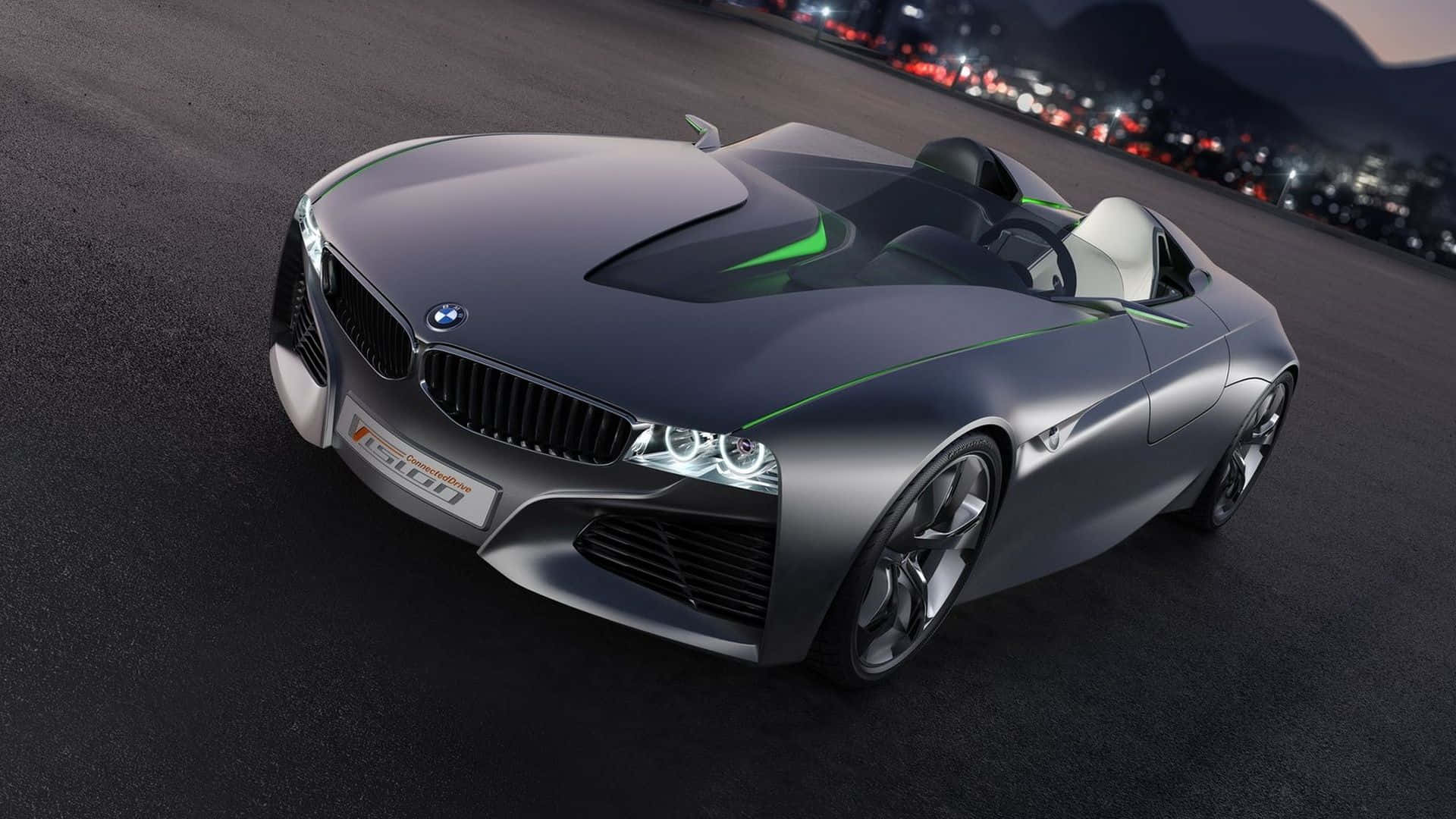 BMW 動圖 桌布 壁紙 — 一輛時尚的銀色BMW概念車，帶有綠色點綴，停在黑暗的道路上，俯瞰夜晚閃爍的城市天際線。