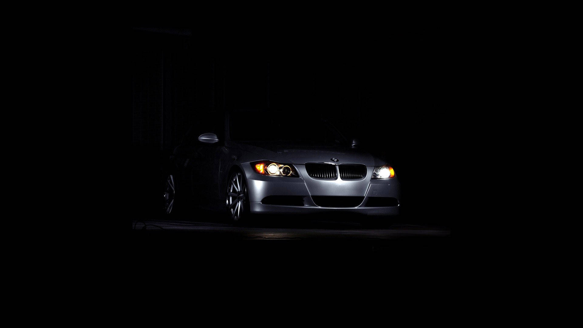 Black Bmw 桌布 壁紙 — 一輛時尚的銀色BMW跑車在漆黑背景下閃耀著亮起的車頭燈。