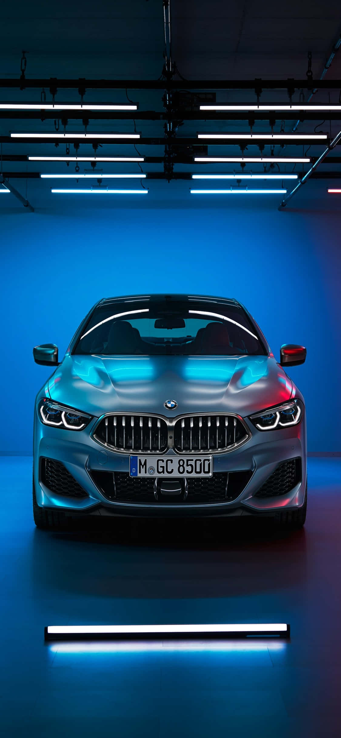 iPhone X Bmw 桌布 壁紙 — 一輛時尚的銀色BMW跑車在簡約車庫環境中，在酷炫的藍色霓虹燈下閃閃發光。